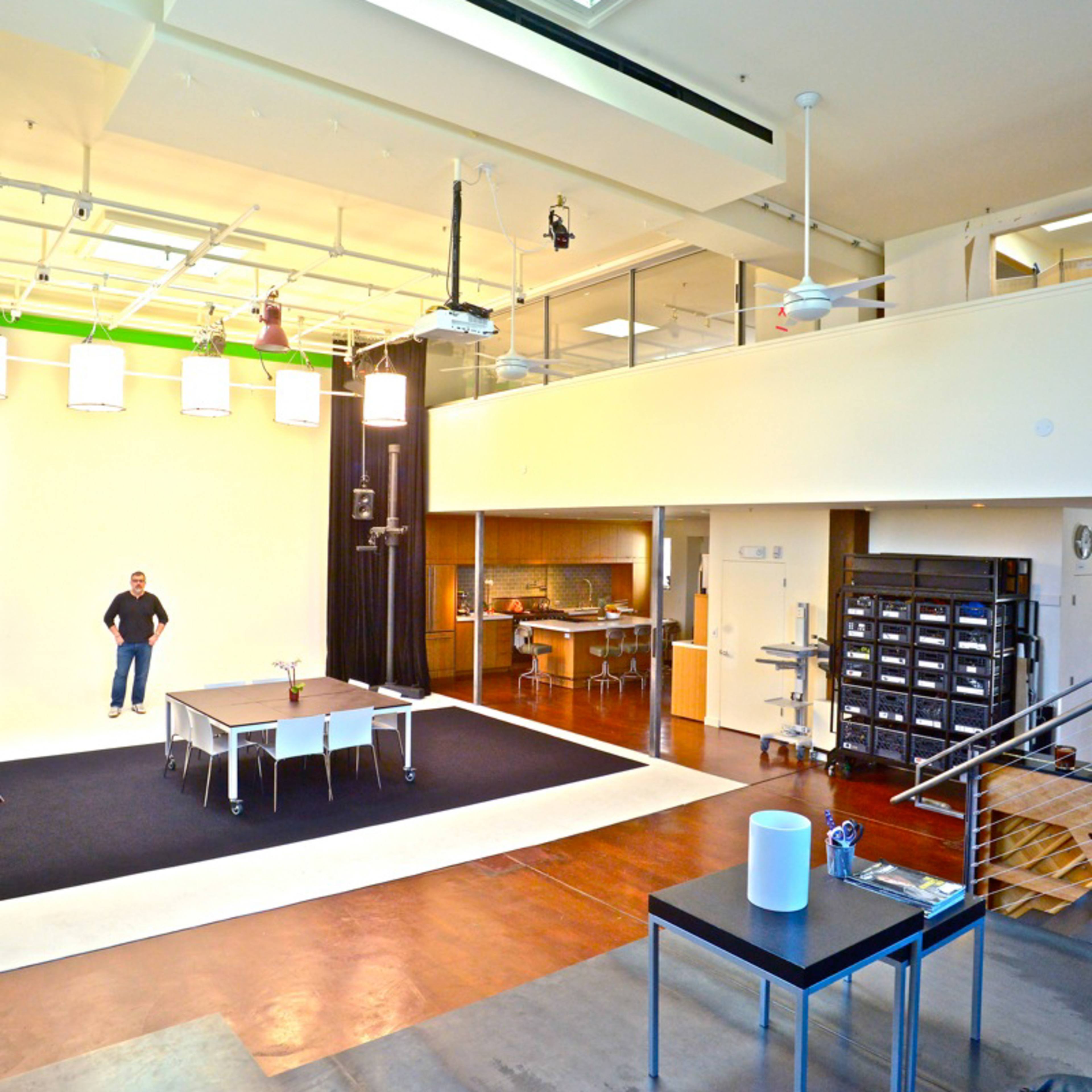 A green screen studio is set up with three red chairs and a small white table in the center.