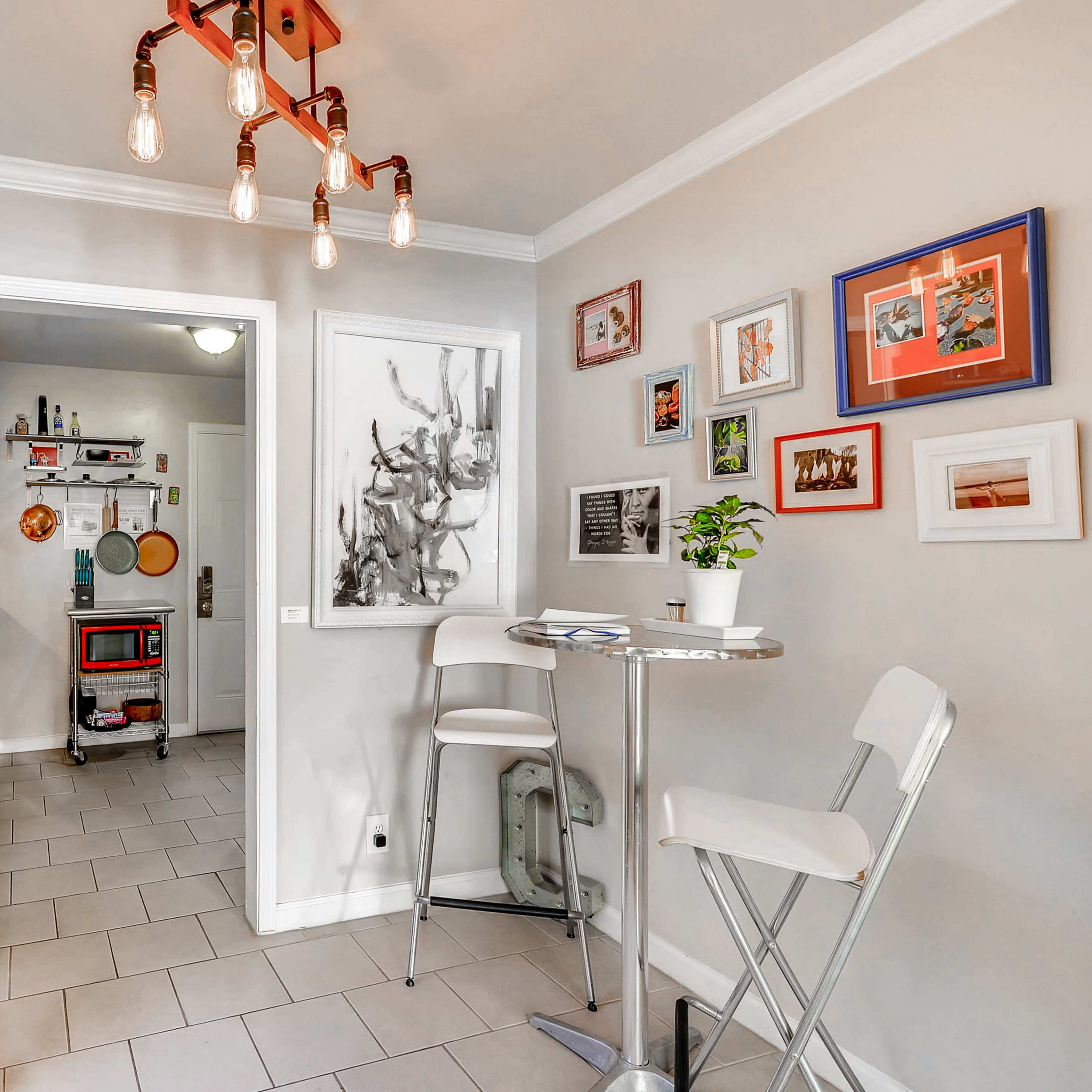 A small dining area with a round table and two white chairs, adjacent to an entryway featuring a red cabinet and various framed pictures on the wall.