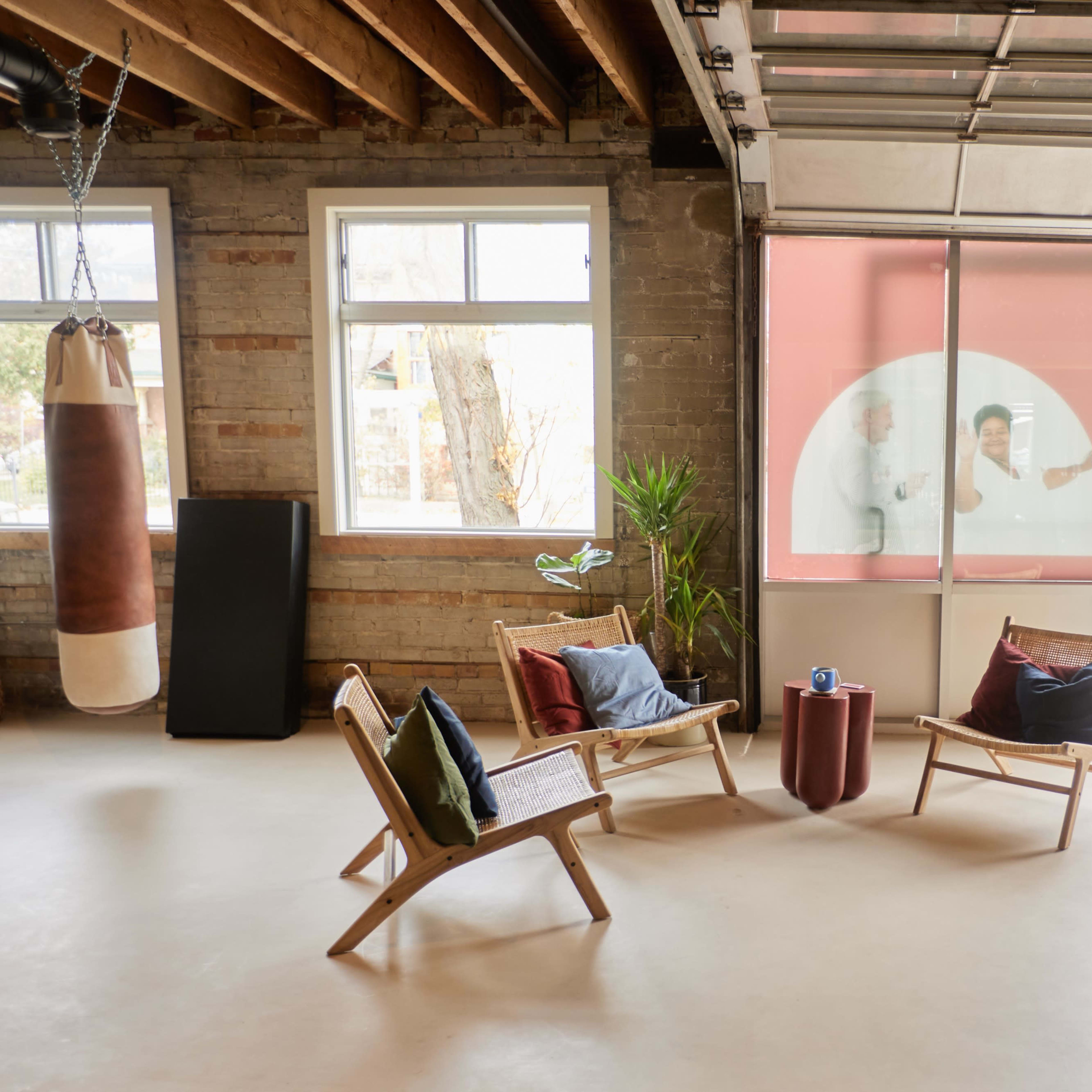 A spacious interior with wooden beams, a punching bag, two chairs with cushions, and a small table, while a window reveals a view of the street outside.