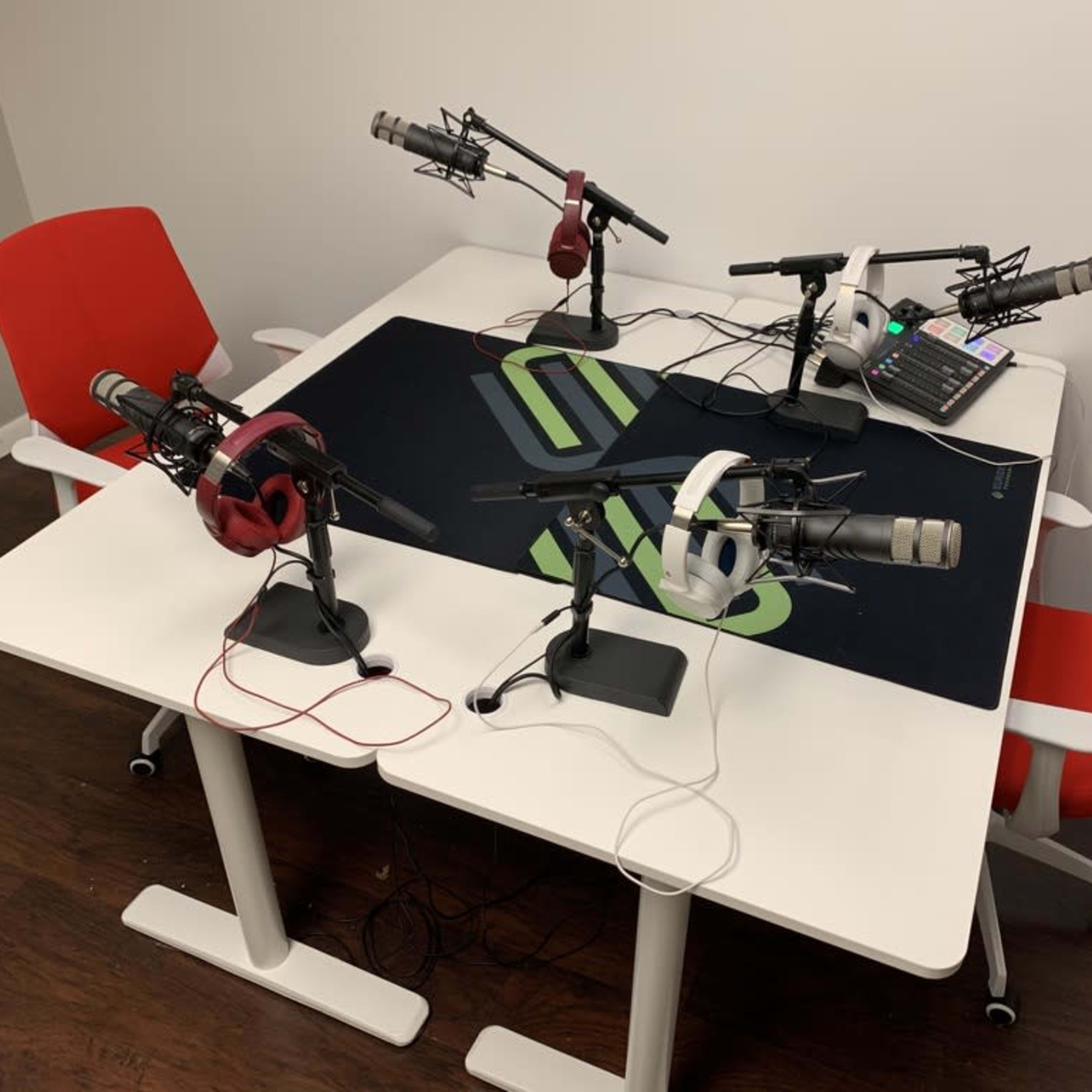A modern podcasting setup featuring four microphones, headphones, and a control panel on a white table with red chairs.