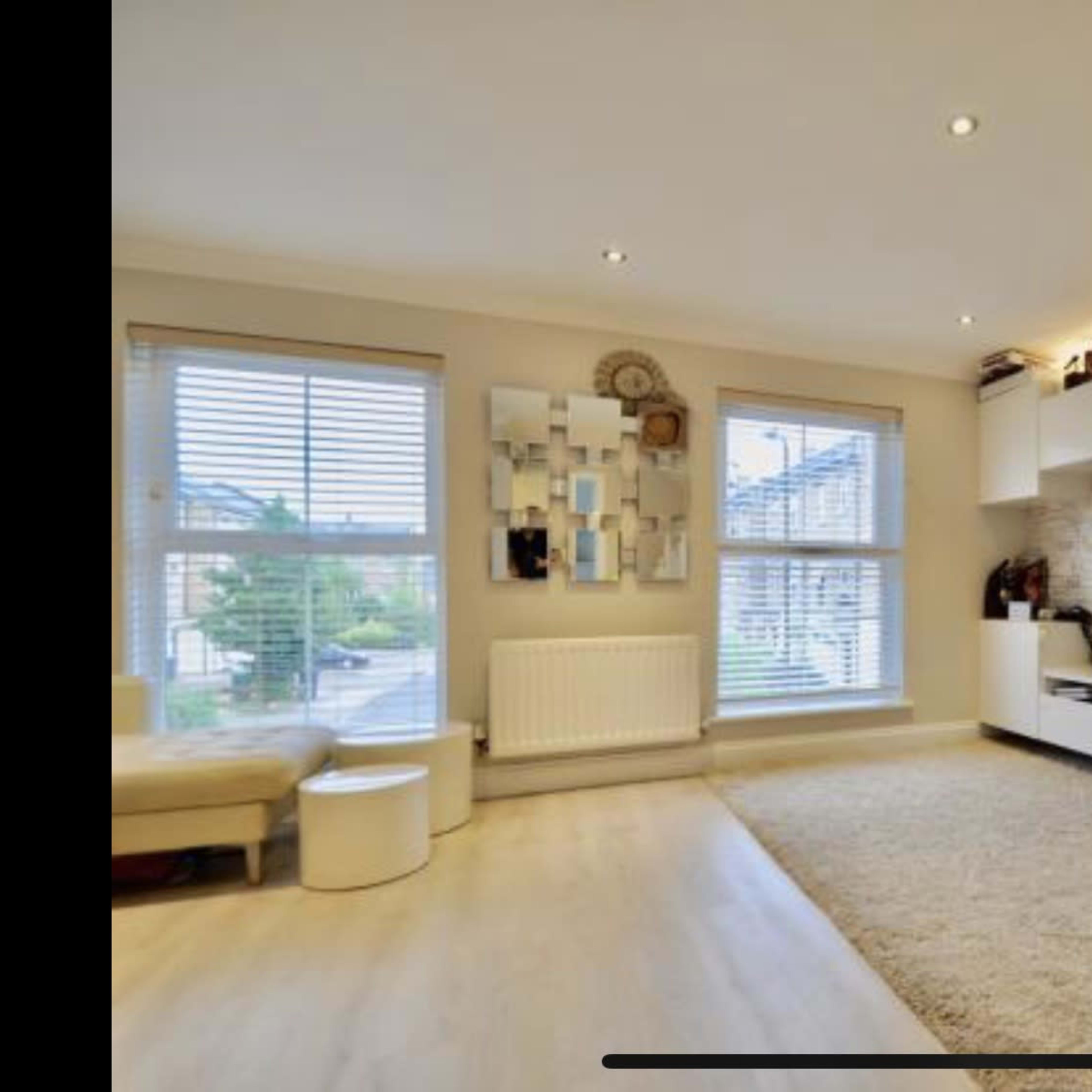 A modern living room with a television mounted on the wall, a plush rug on the floor, and a large window with blinds.