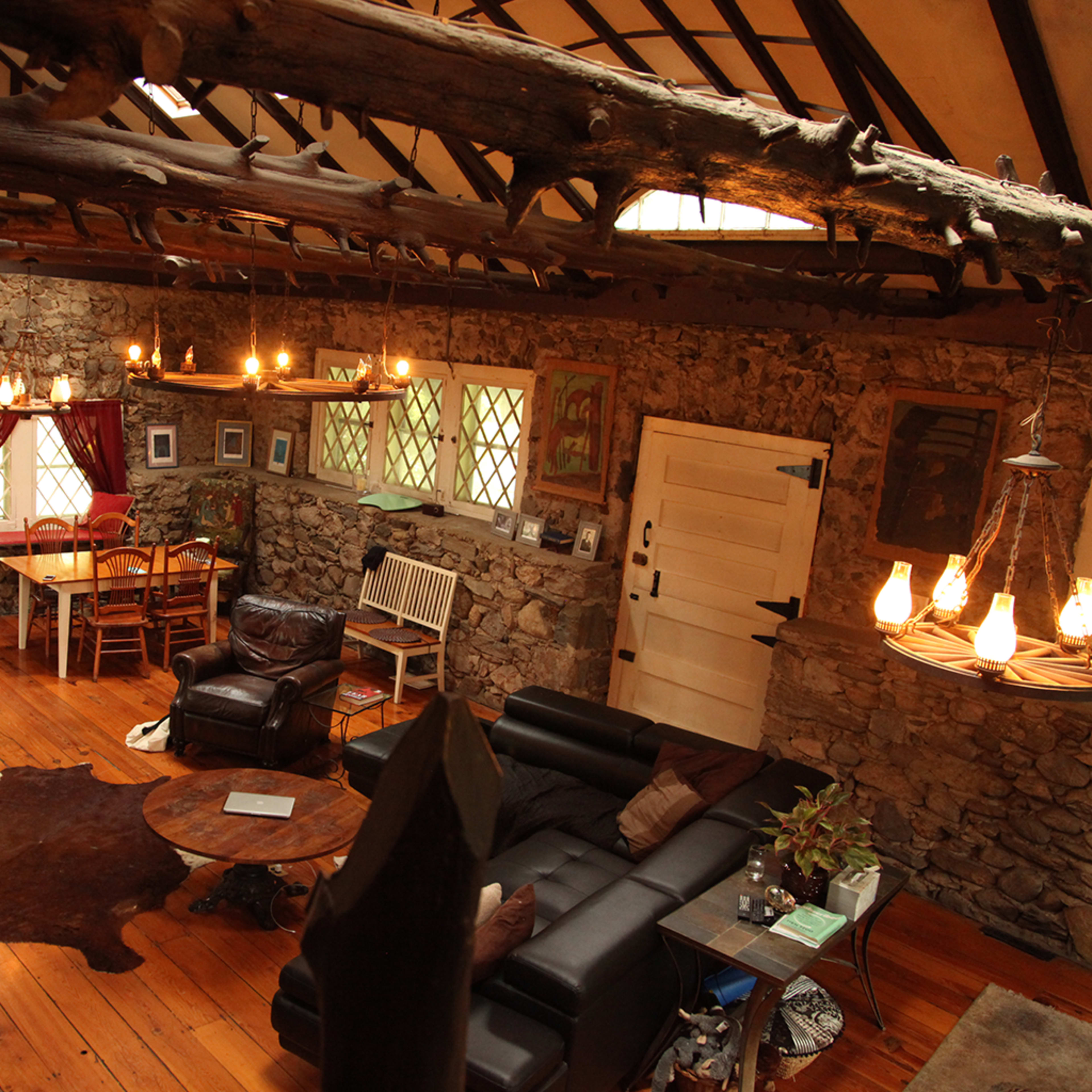 A rustic interior of a stone cottage with wooden beams, a leather sofa, a dining area, and decorative wall art.