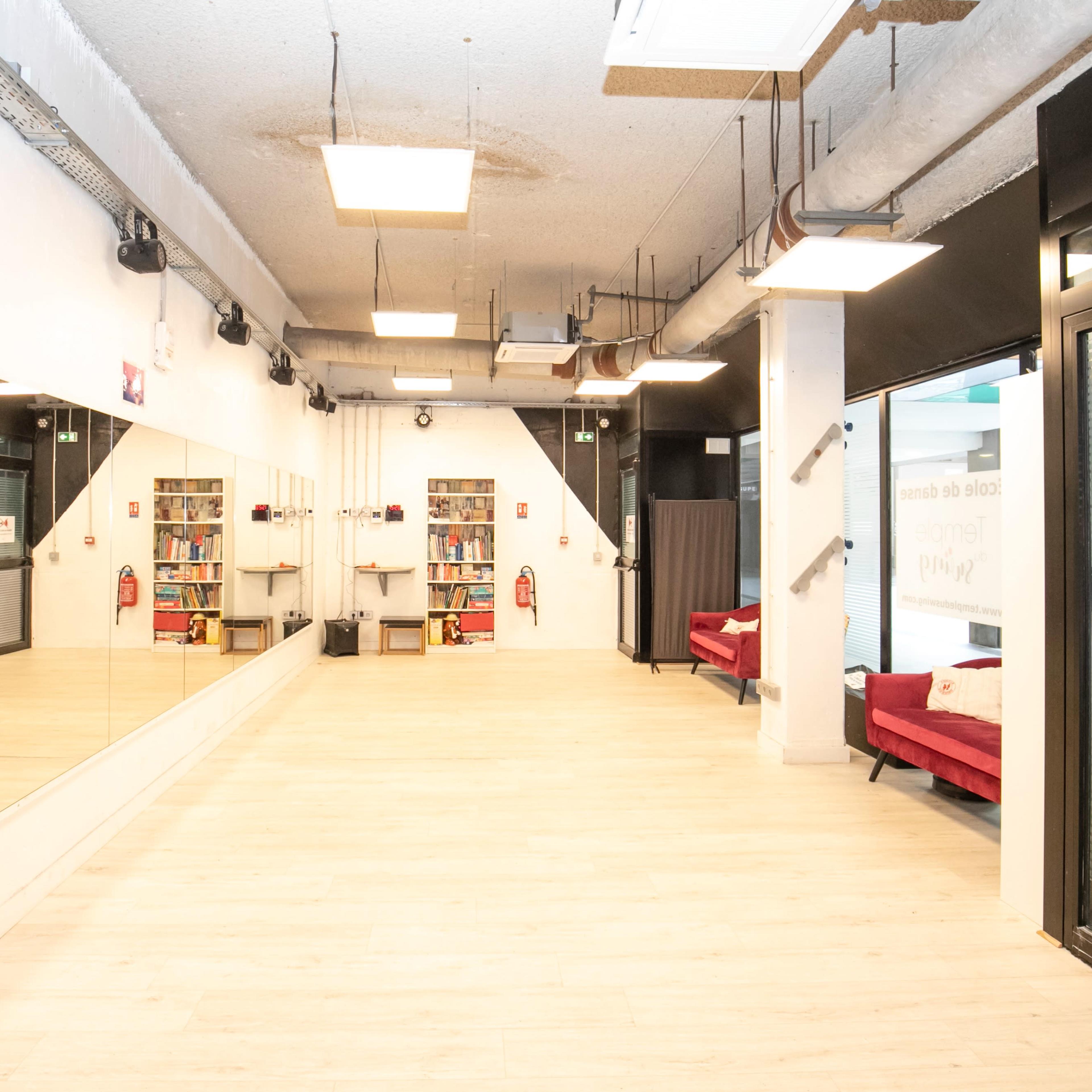 A spacious room with wooden flooring, large mirrors on one wall, red sofas, and shelves filled with books.