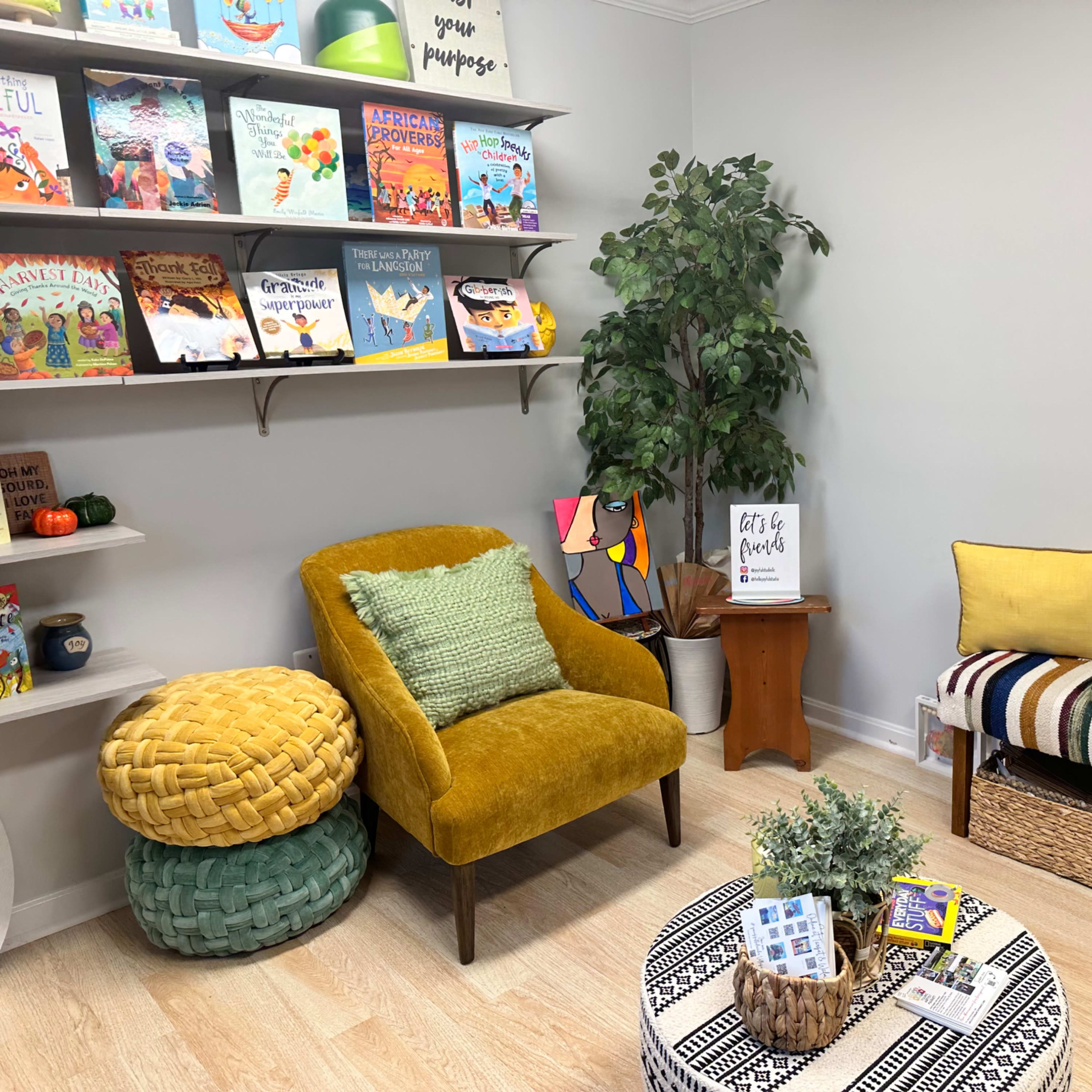 A cozy reading nook with two chairs, a small round table, shelves filled with colorful books, and decorative plants.