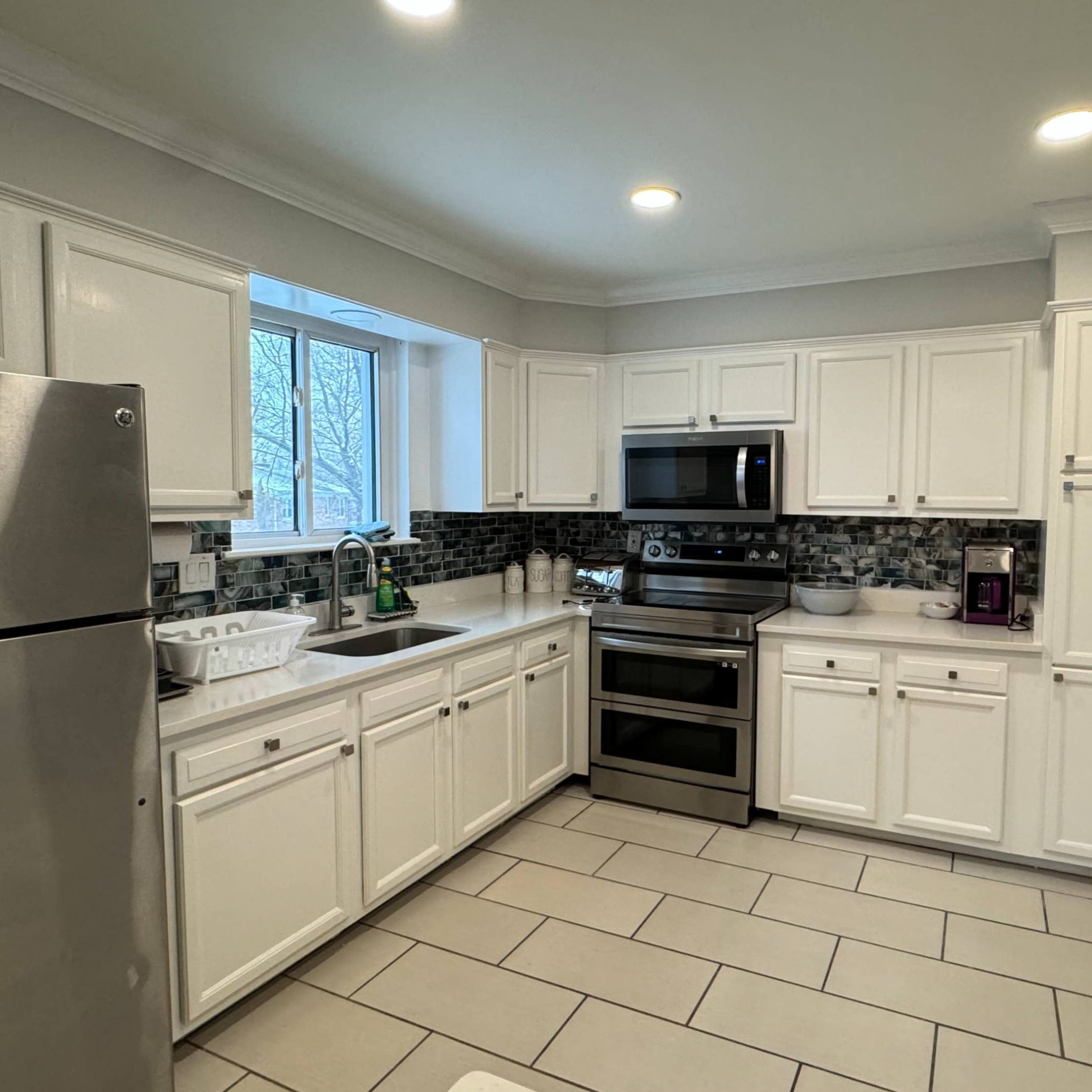 A modern kitchen featuring white cabinetry, stainless steel appliances, a central island, and tile flooring.