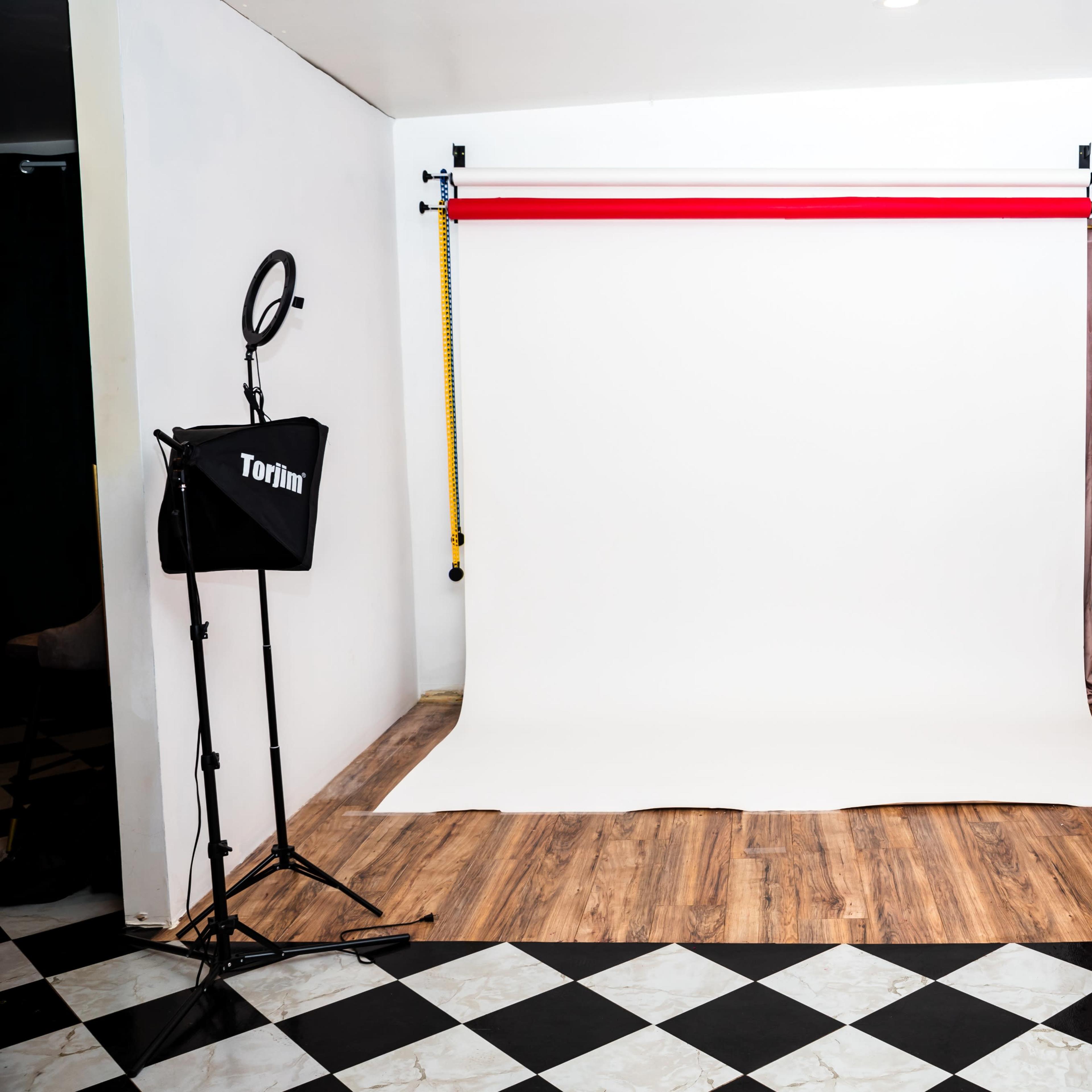 A photography studio with a white backdrop, lighting equipment, and a wooden floor.
