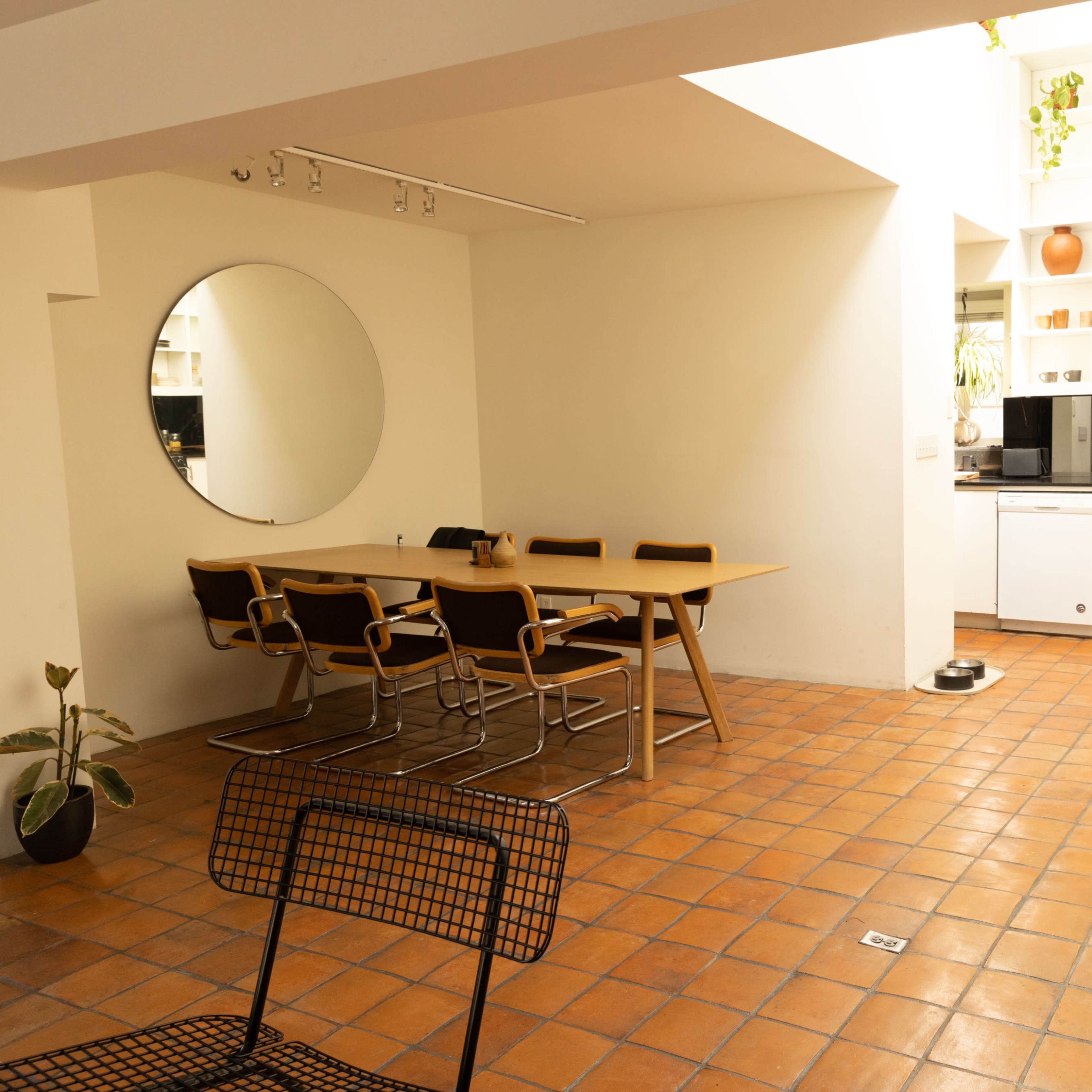 A spacious kitchen and dining area featuring a round mirror, a wooden table with seating, and a white cabinetry setup with a black countertop.
