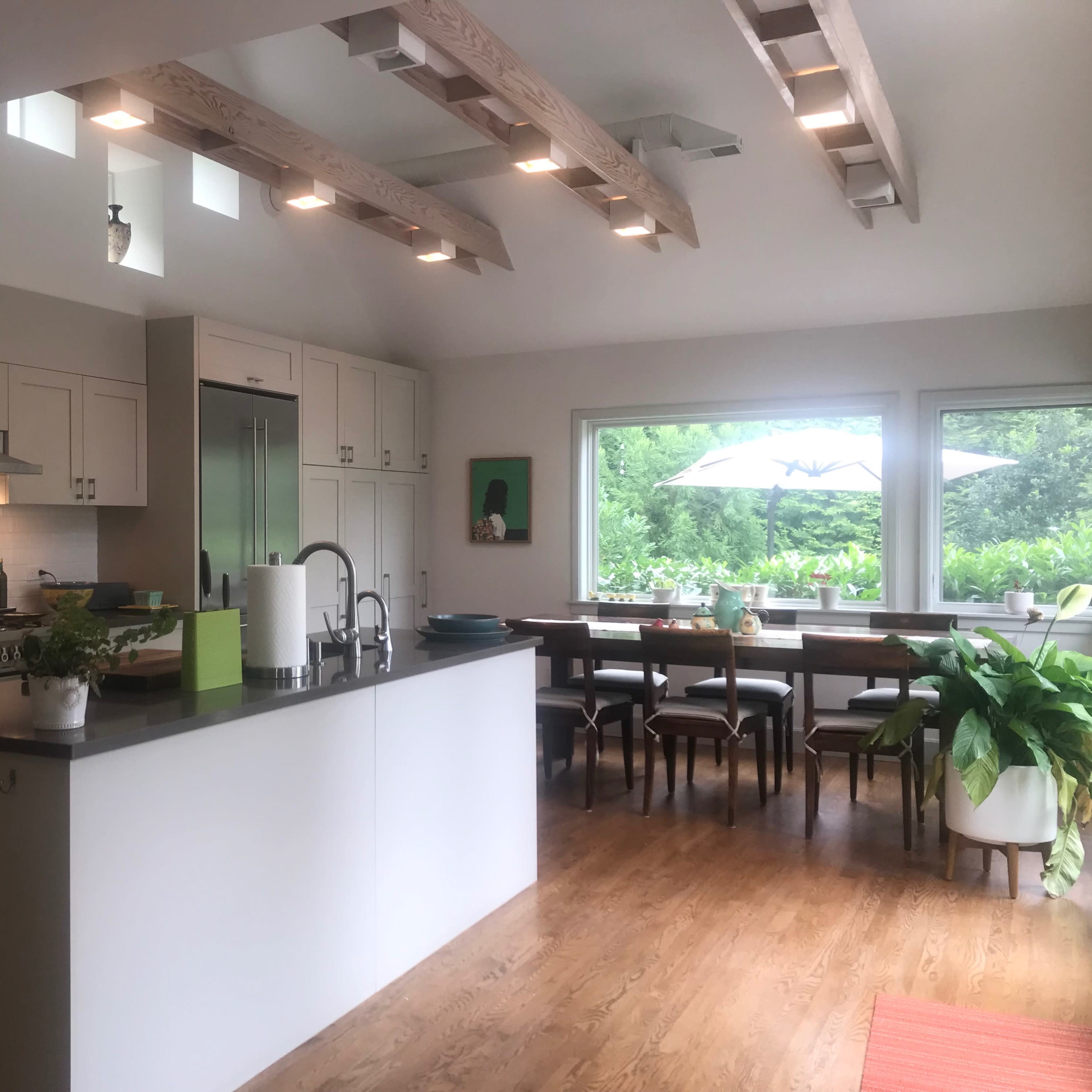 A modern kitchen with an island, stainless steel appliances, and a dining area featuring a large table near a window that overlooks a green landscape.