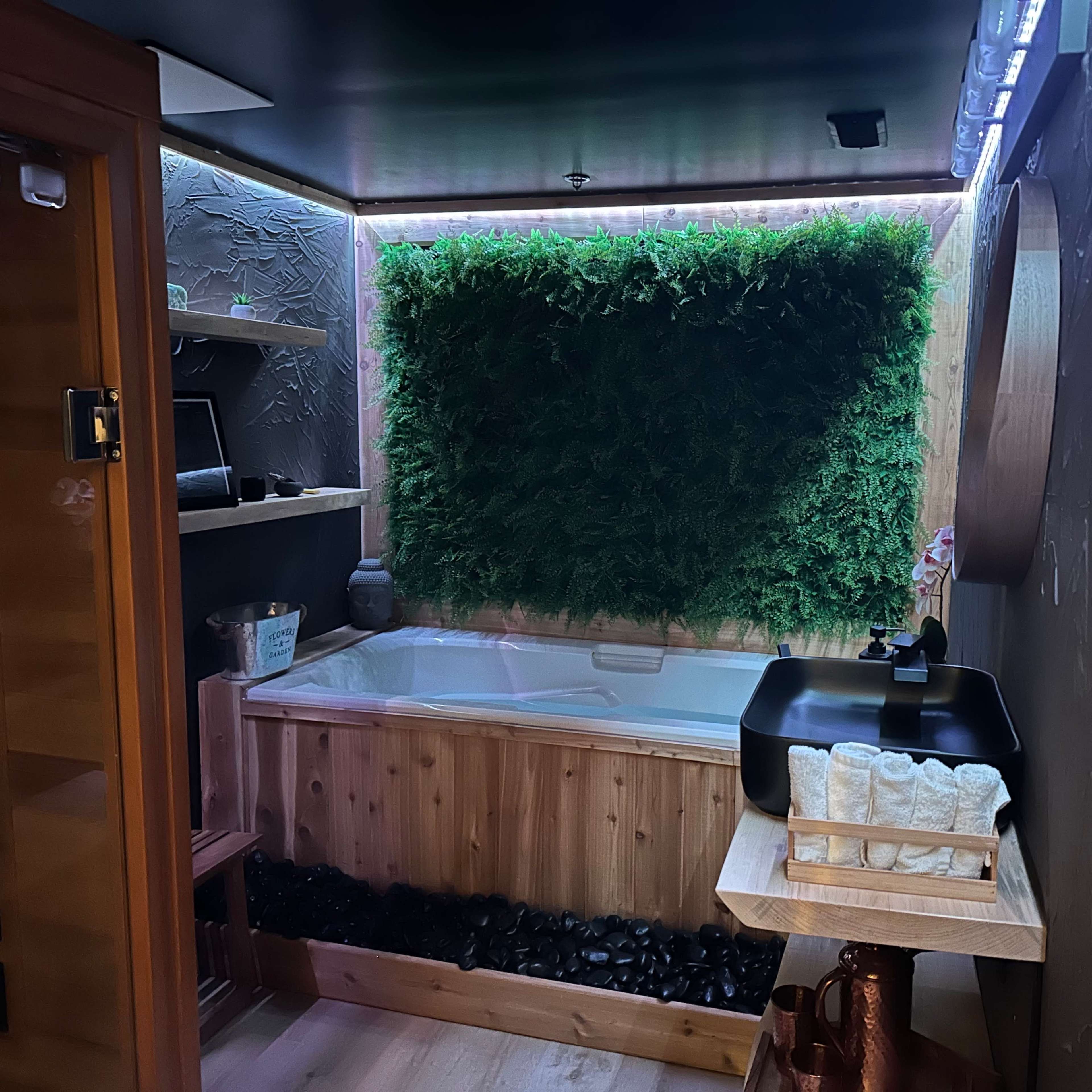 A modern spa room featuring a wooden hot tub surrounded by a green moss wall and minimalistic decor.