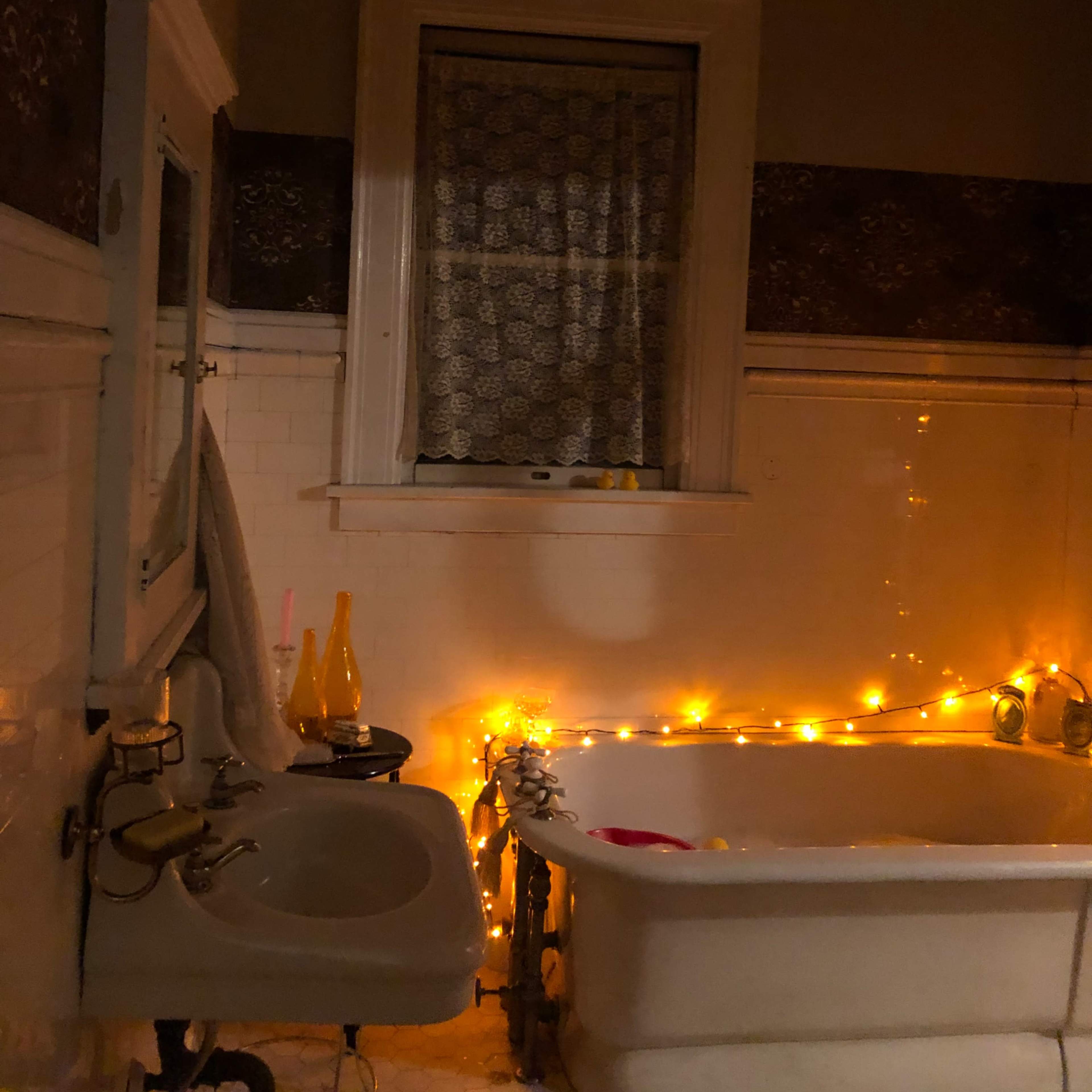 A bathroom with a clawfoot tub, a sink, and warm string lights illuminating the space.