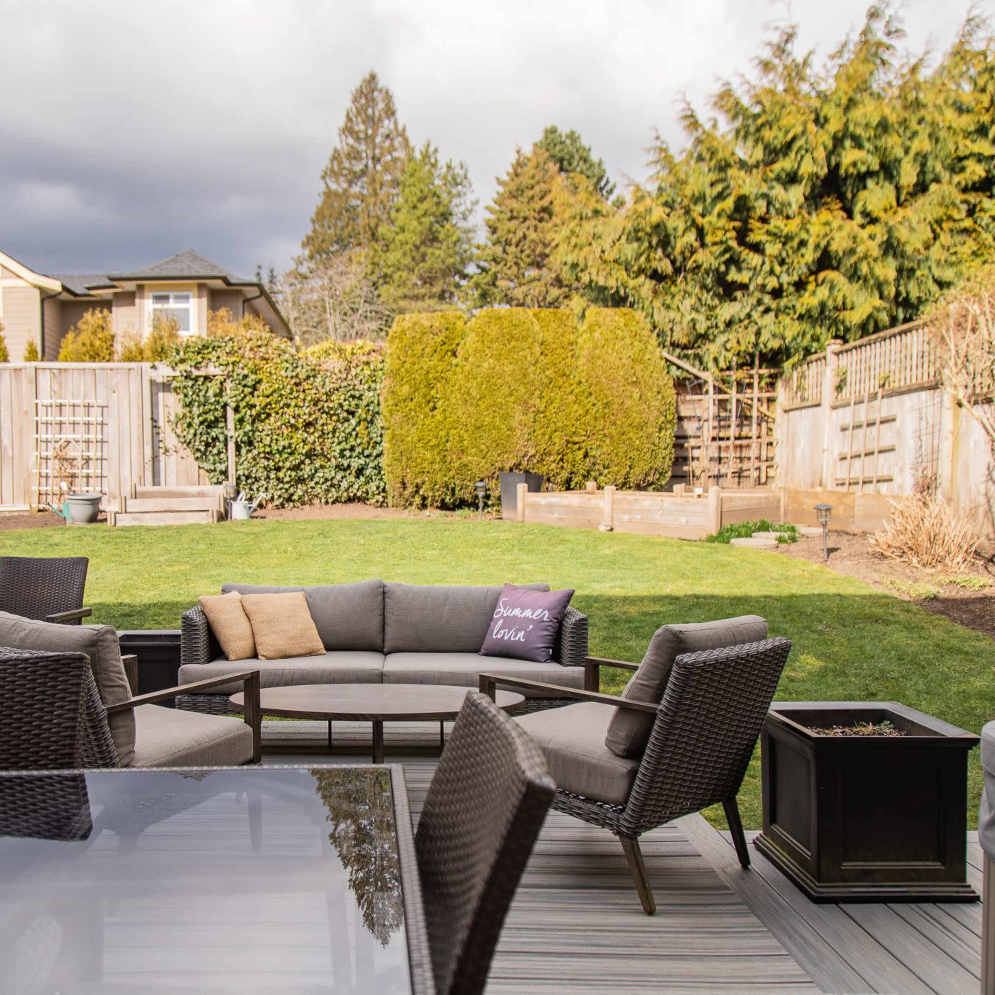 A patio area features a sectional sofa and chairs, with a lawn and landscaping visible in the background under a cloudy sky.