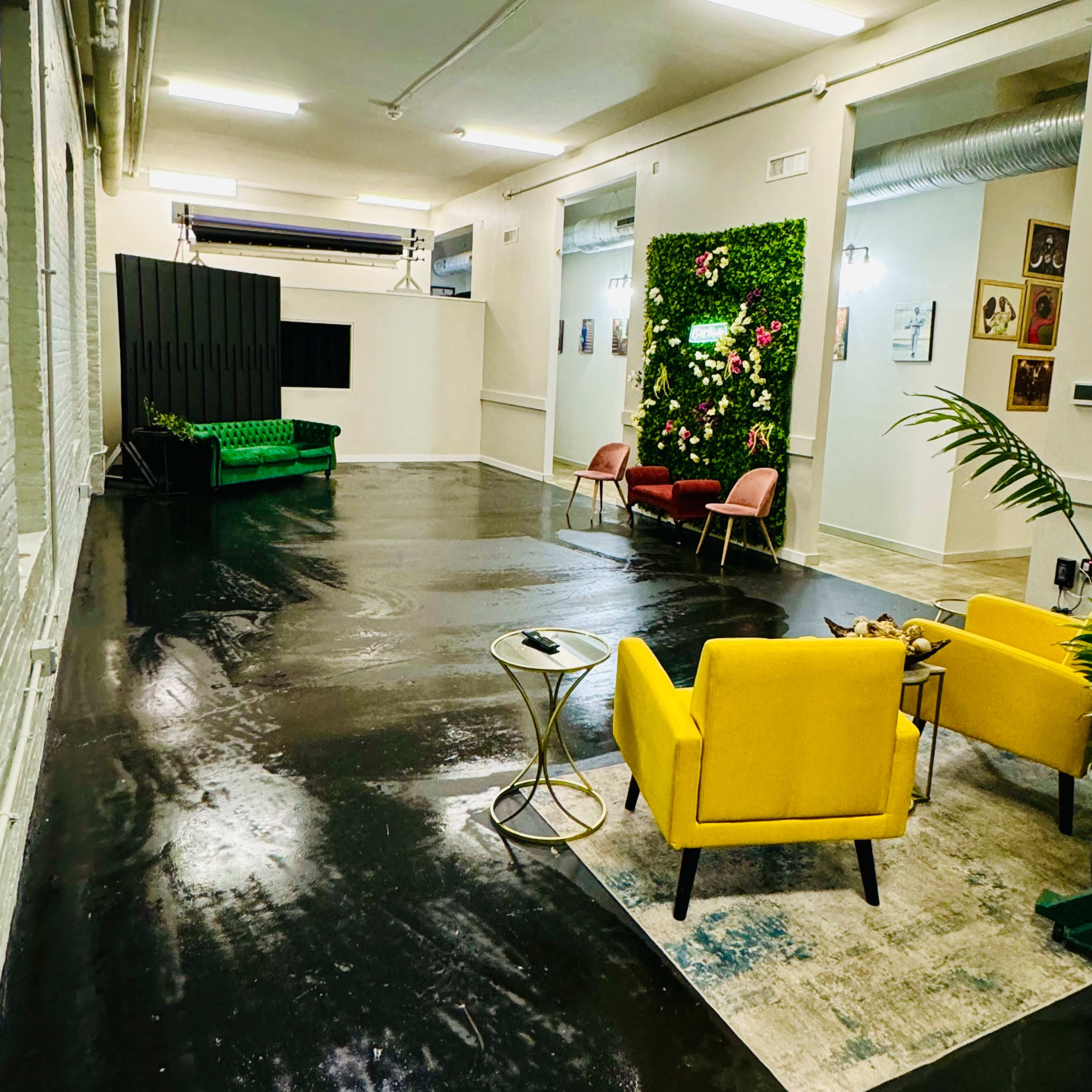 A spacious interior with a polished black floor, featuring colorful seating areas and a wall adorned with plants and flowers.