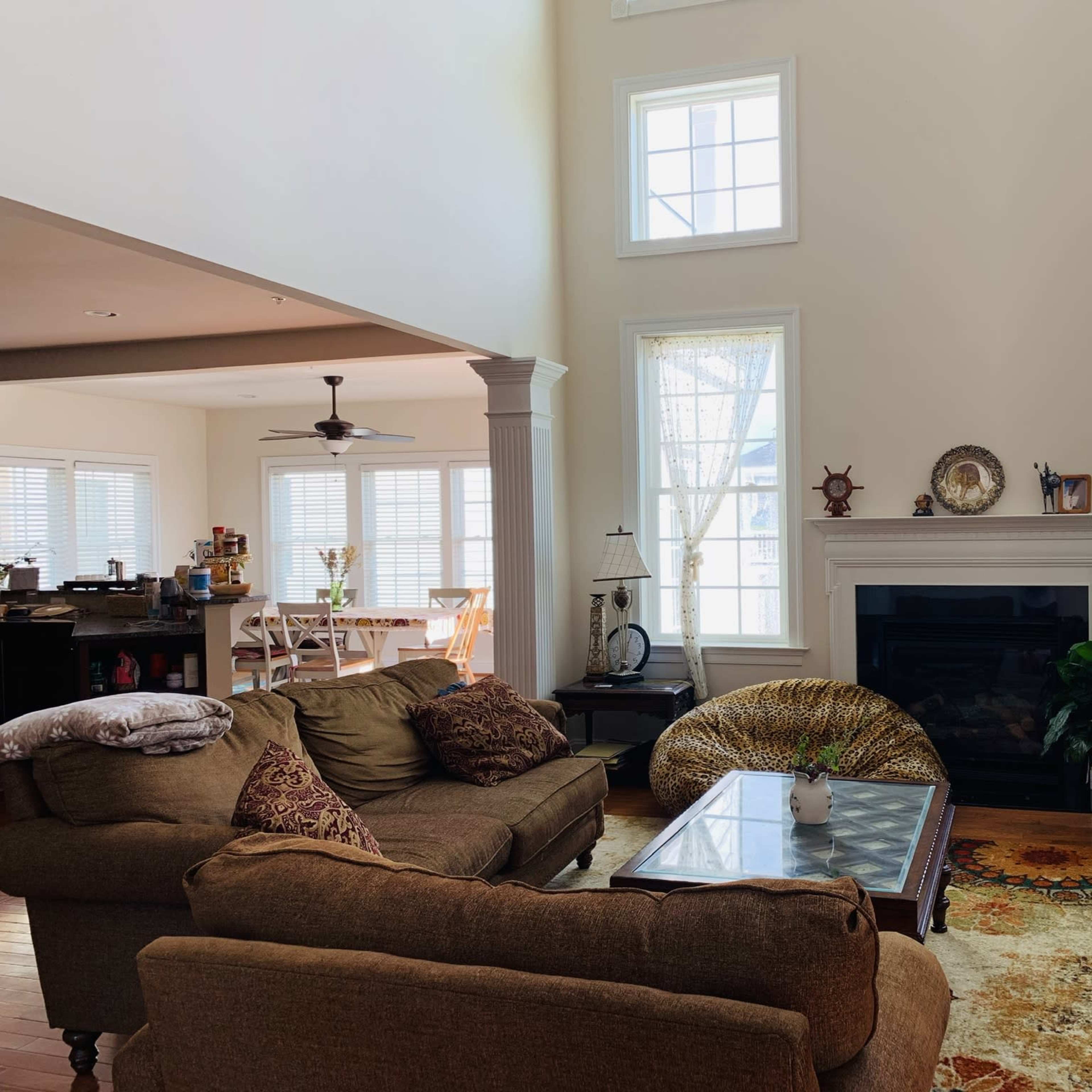 A spacious living room features a large sofa, a glass coffee table, and windows that allow natural light to fill the space.