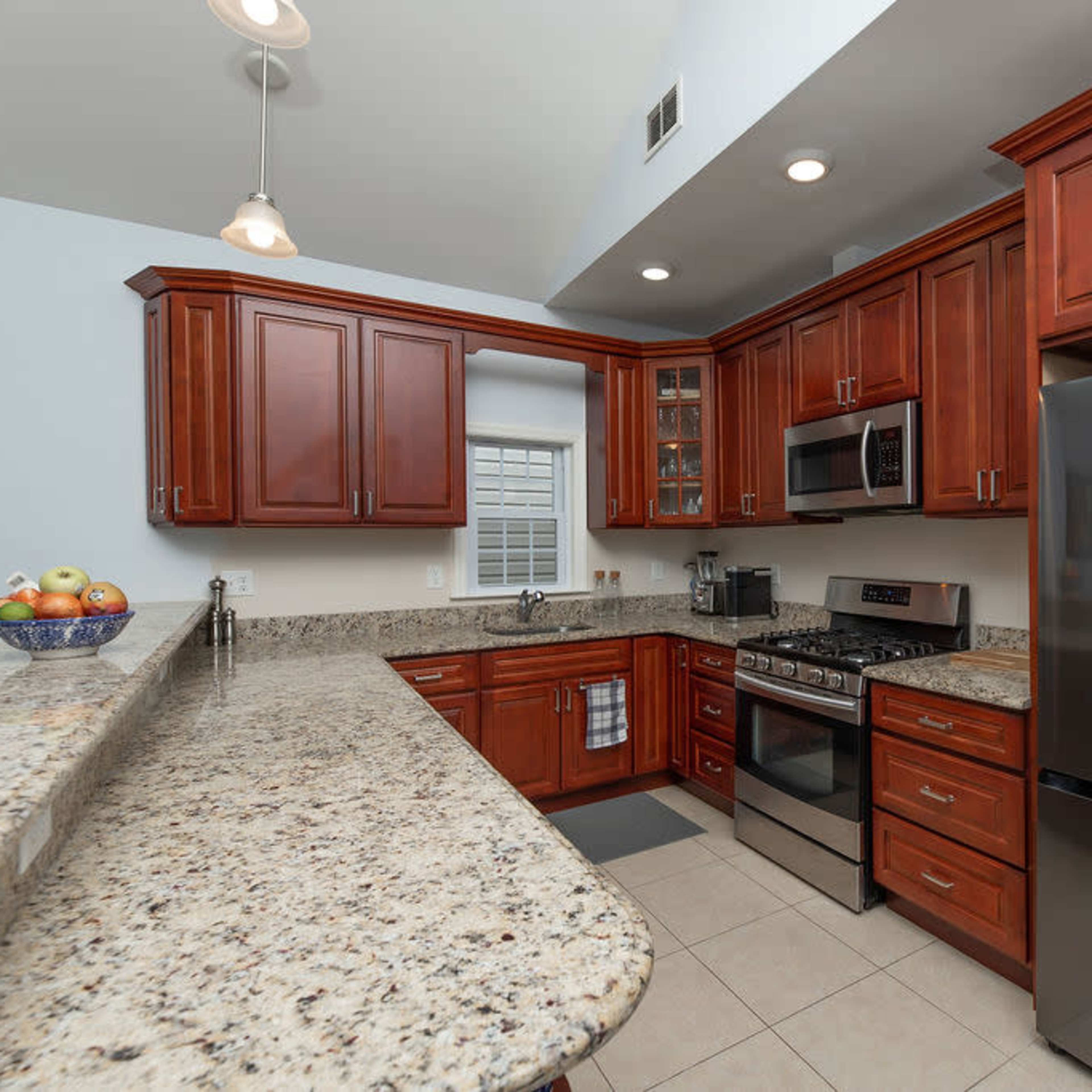 The kitchen features dark wooden cabinets, granite countertops, stainless steel appliances, and a central island with a bowl of apples.