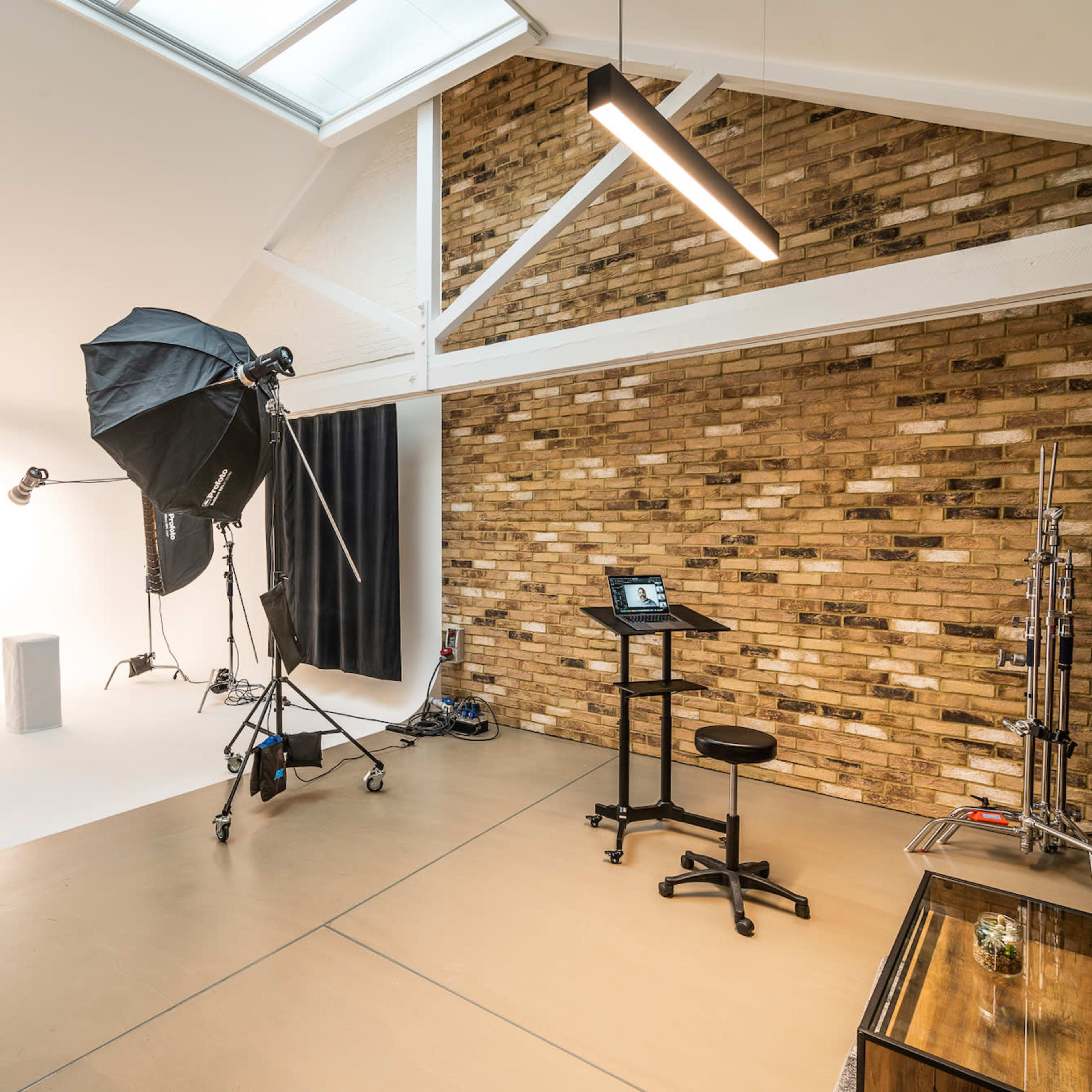 A photography studio with a light setup, a stool, and a backdrop against a brick wall.