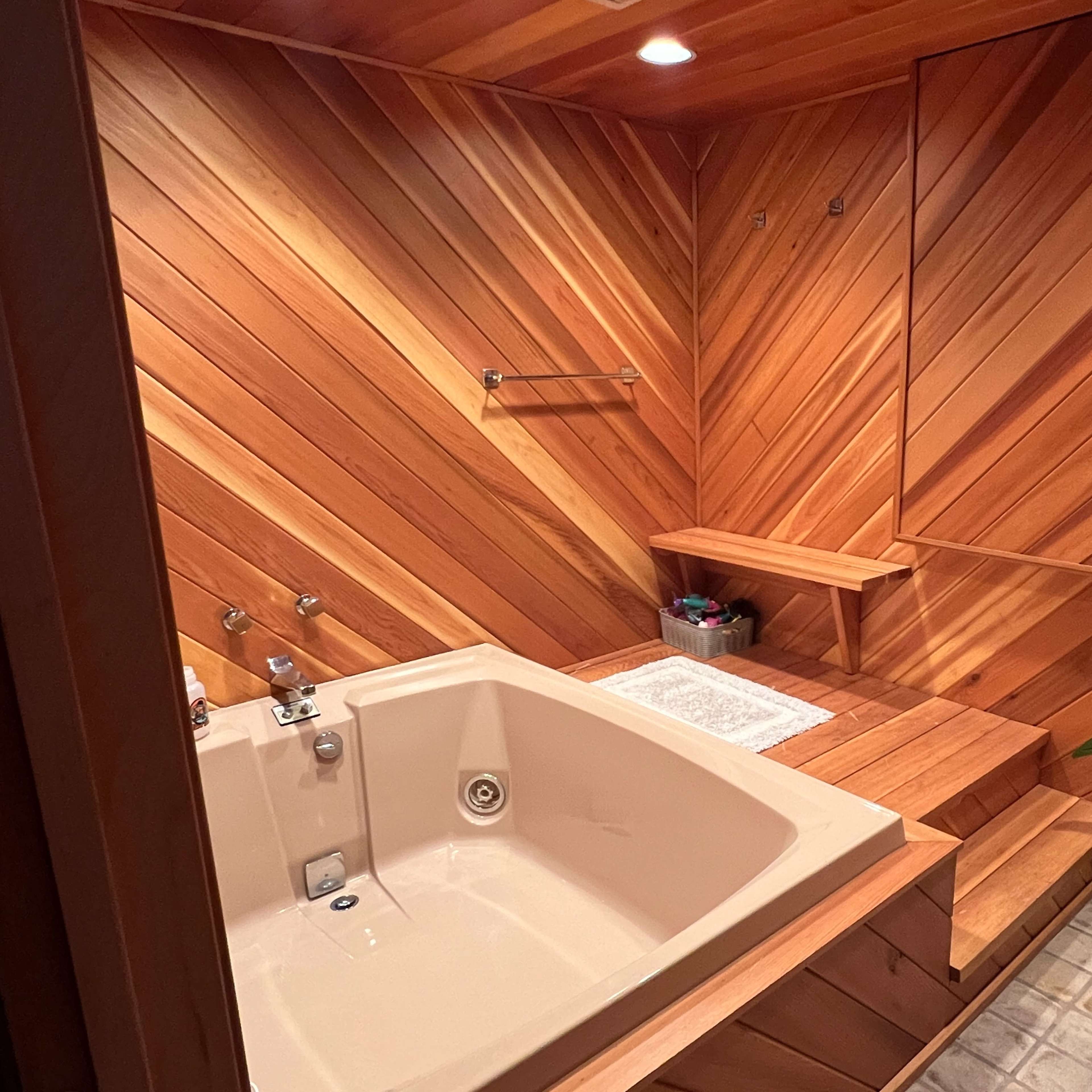 A wooden-paneled bathroom featuring a large spa tub, a bench, and a potted plant.