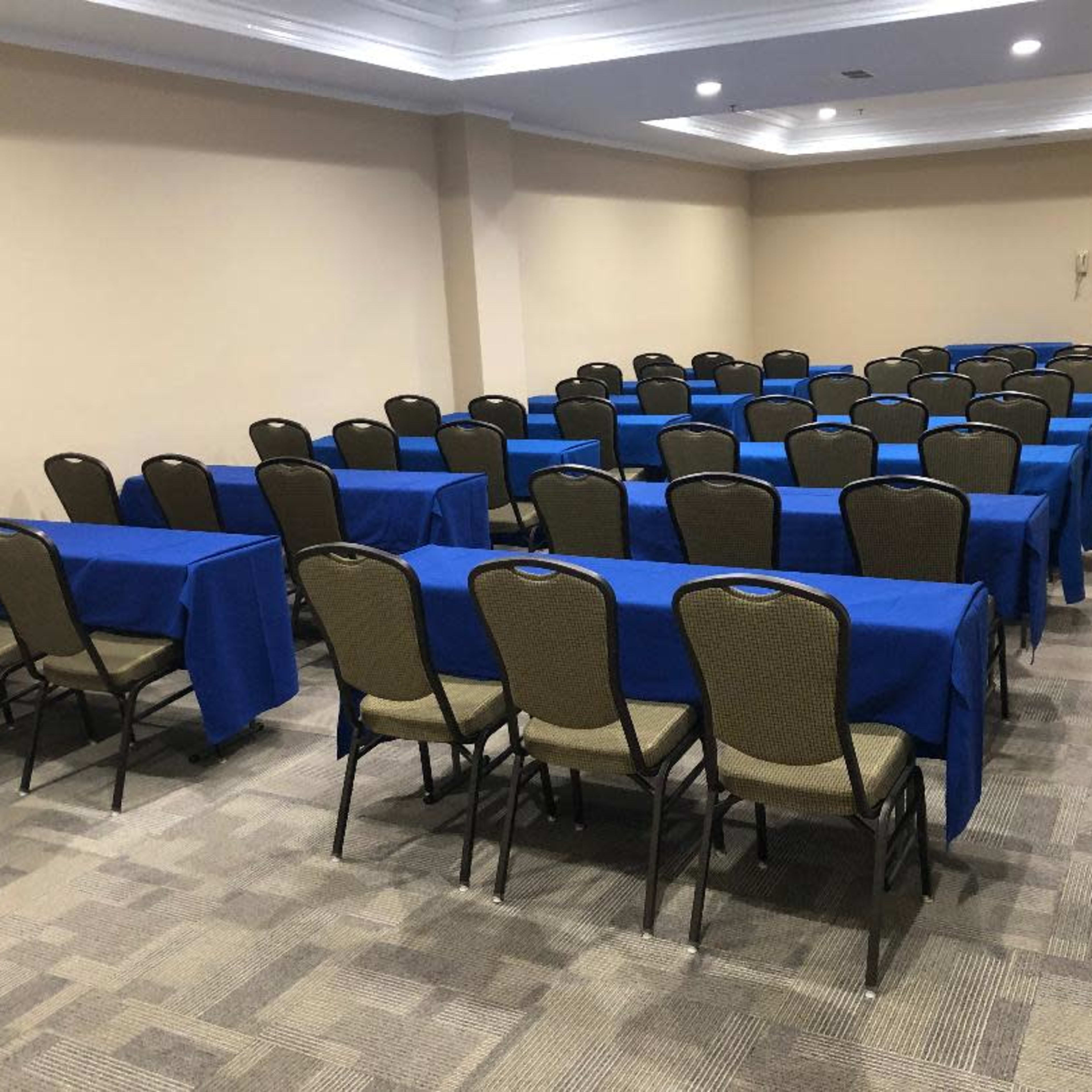 A conference room is set up with several rows of blue-covered tables and chairs arranged for attendees.