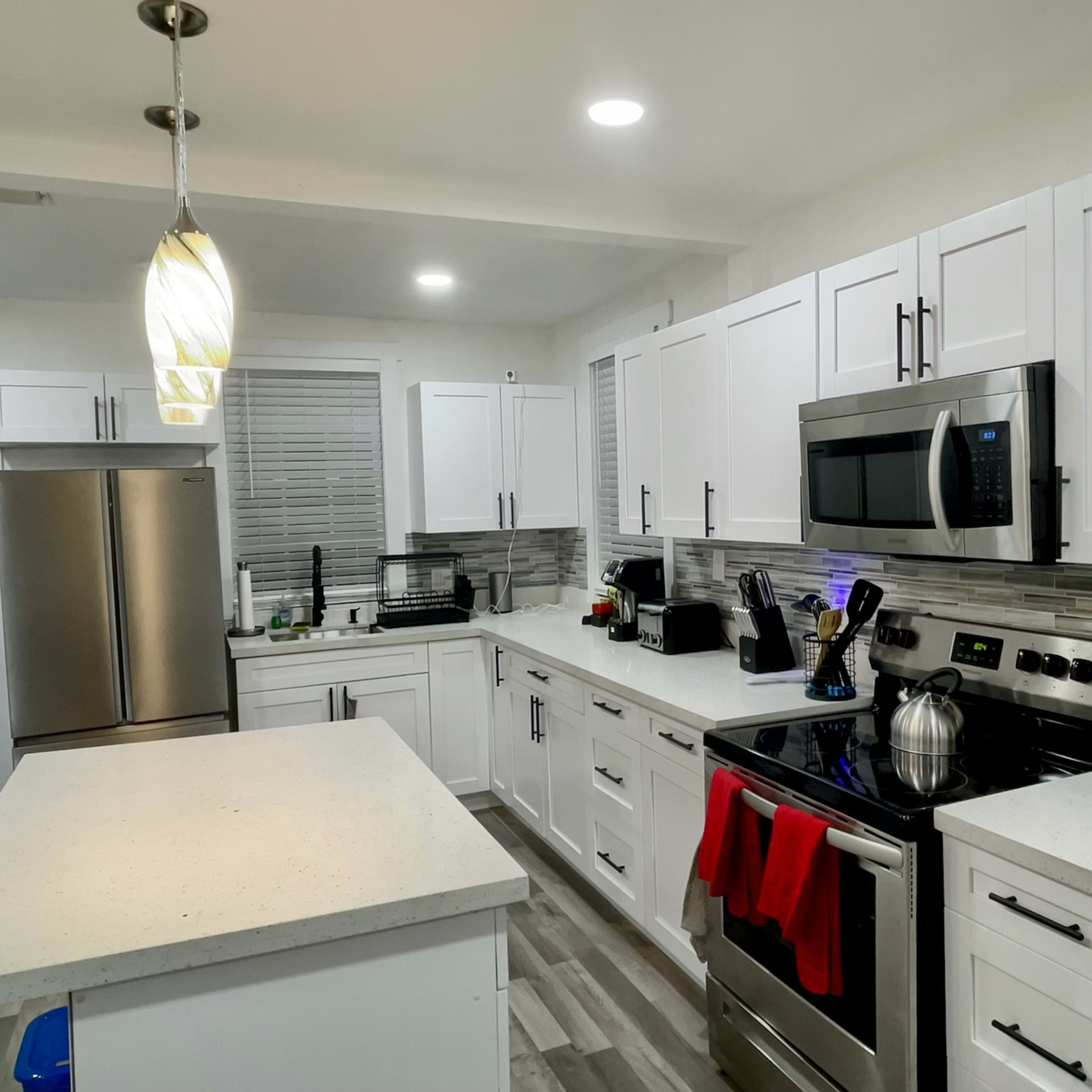 A modern kitchen features white cabinetry, stainless steel appliances, and a central island with a light fixture overhead.