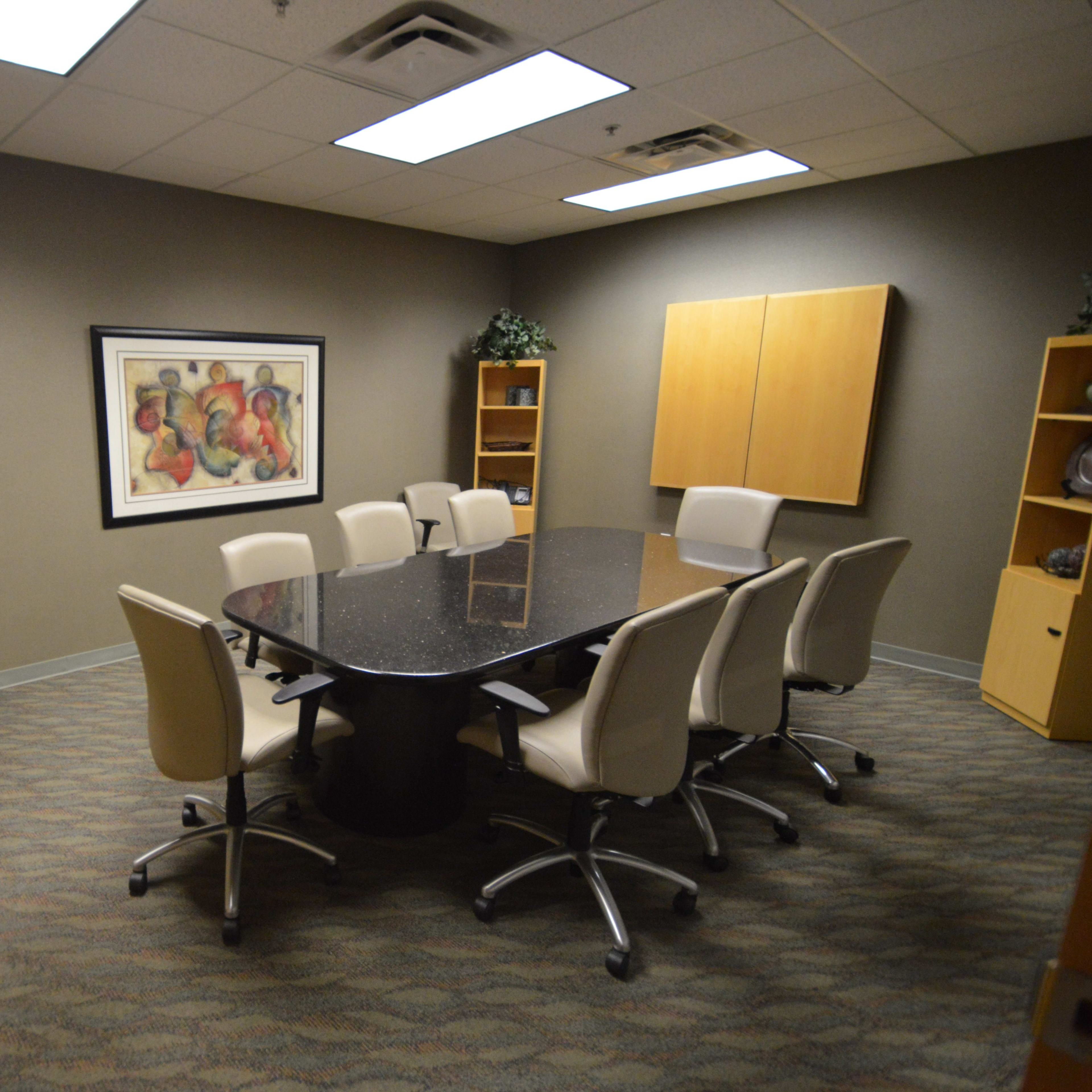 A conference room features a large black table surrounded by eight chairs, flanked by cabinets and a decorative artwork on the wall.