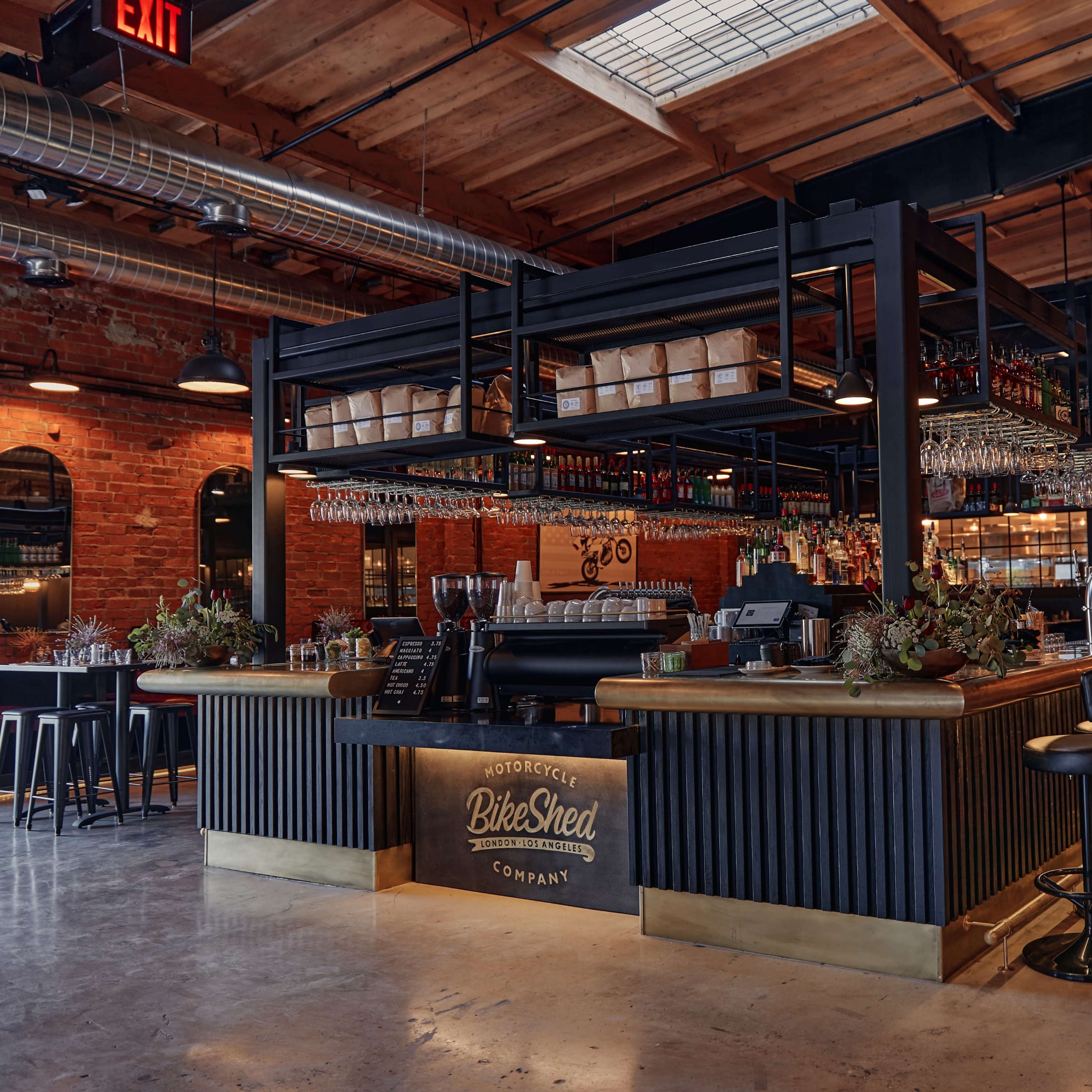 A modern bar area with a wooden counter, high stools, and a background of exposed brick walls and industrial-style lighting.