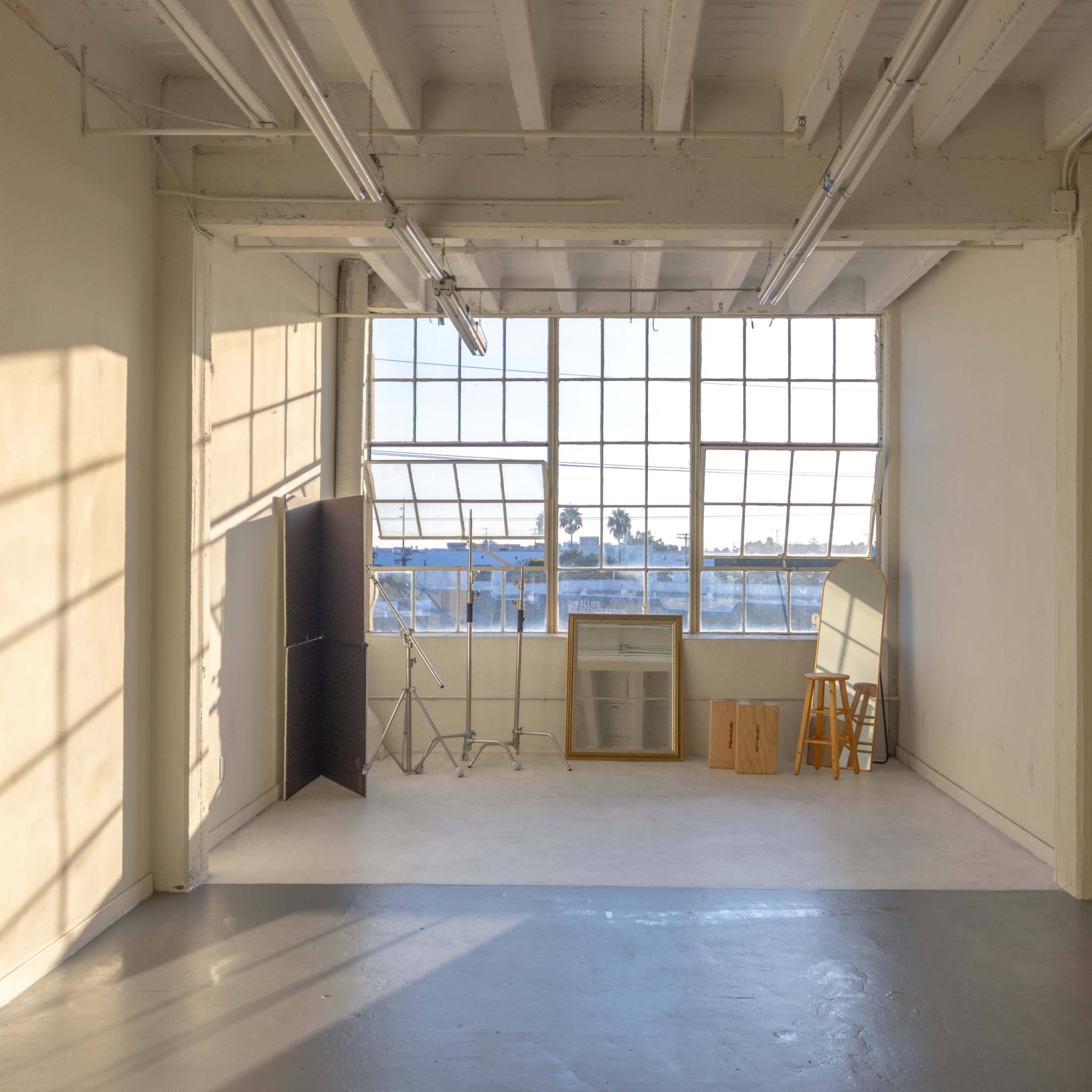A spacious, empty room with large windows allowing natural light to stream in and a few pieces of furniture placed against the walls.