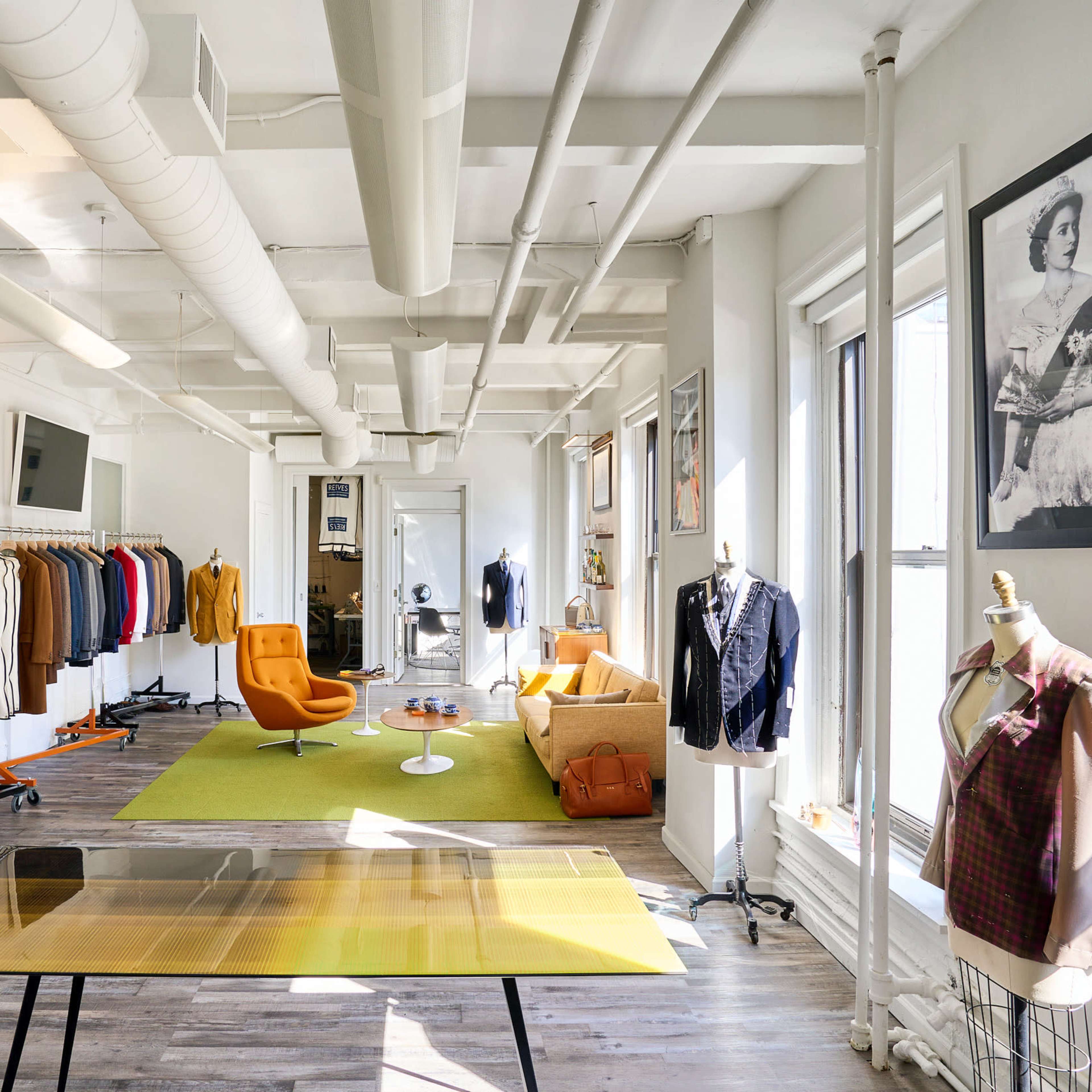 A bright, modern clothing store features a variety of garments displayed on racks, an orange chair, and large windows letting in natural light.