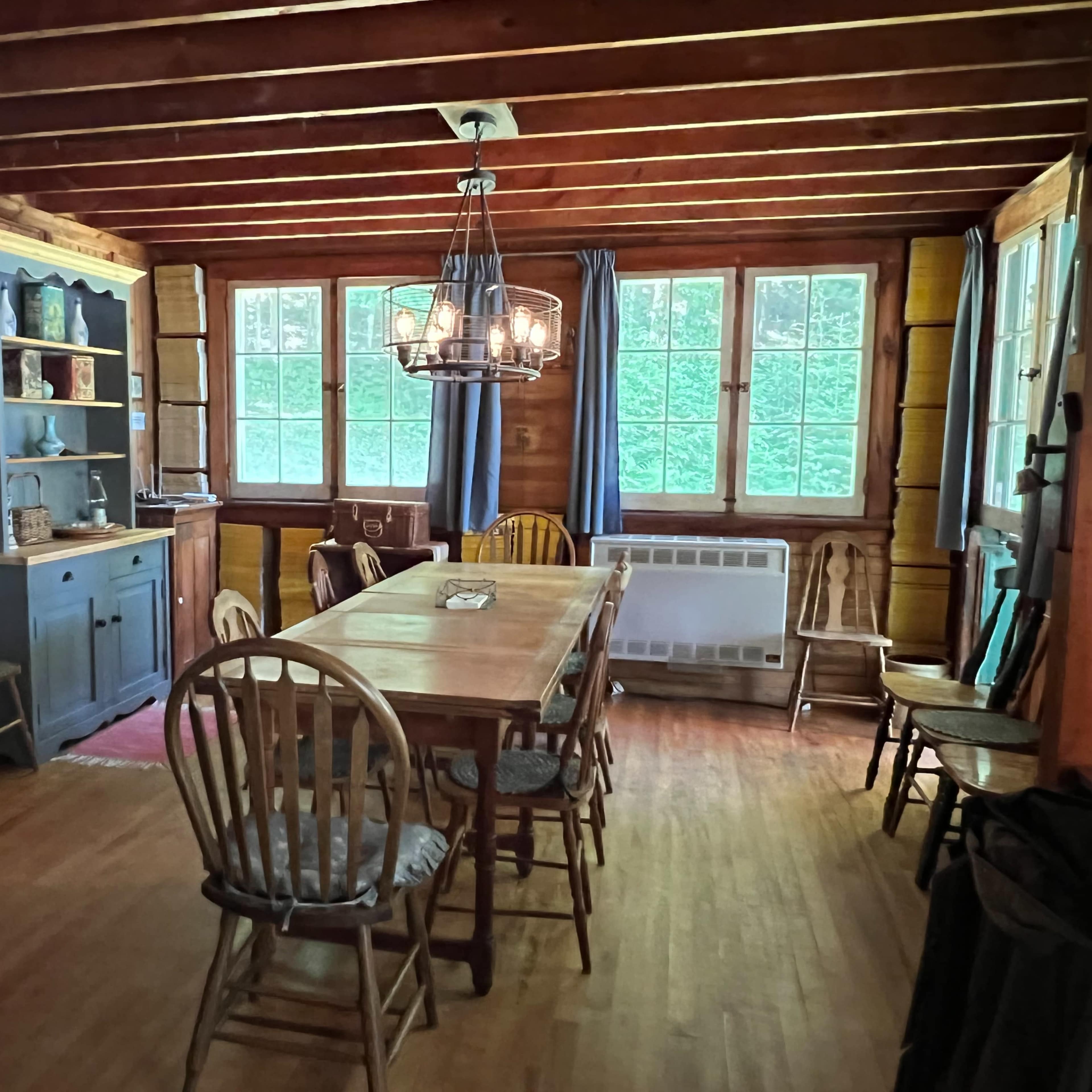 A rustic dining room with wooden walls, a large table surrounded by chairs, and a side cabinet filled with decorative items.