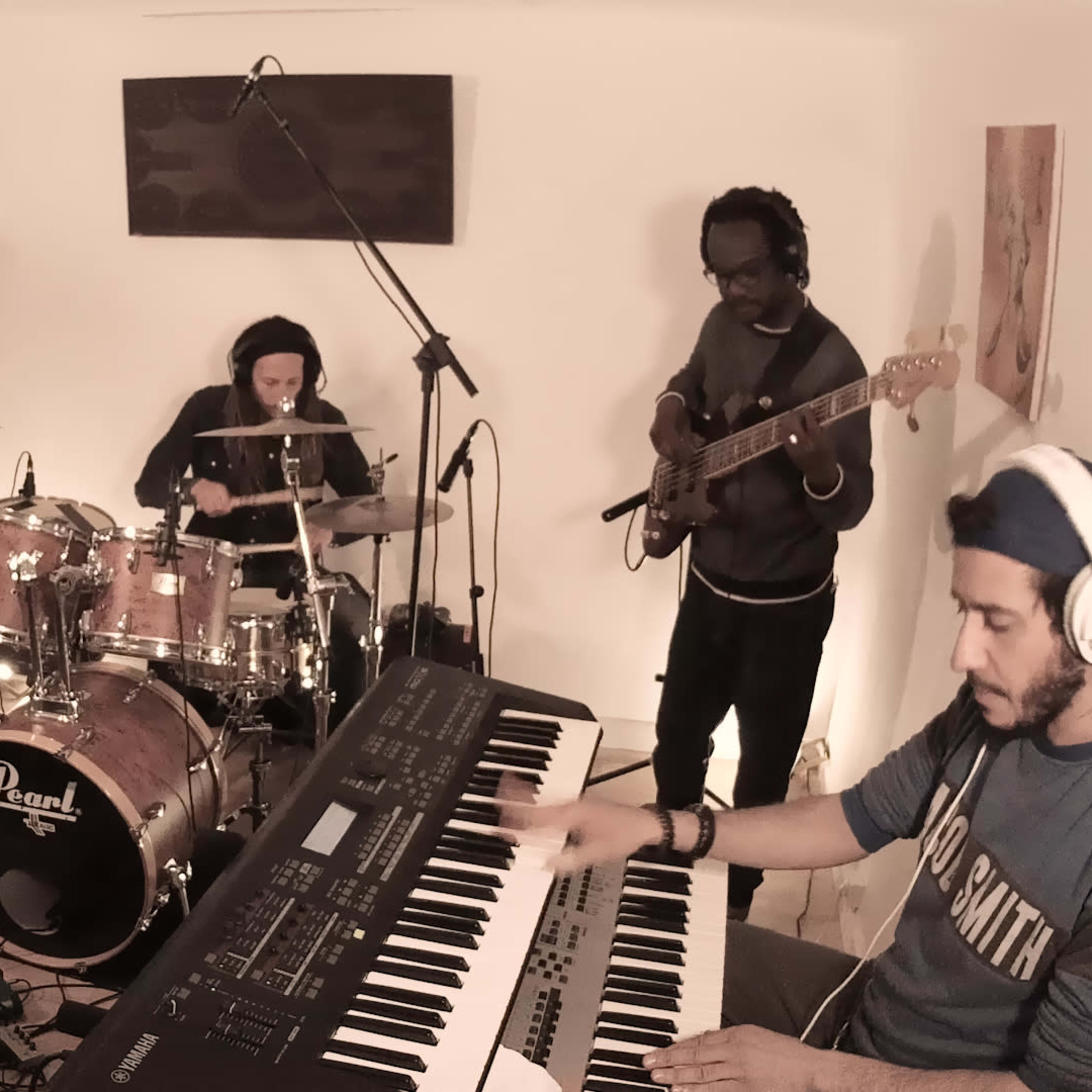 A group of musicians performs together in a studio, with a vocalist, guitarists, a bassist, a drummer, and a keyboardist.