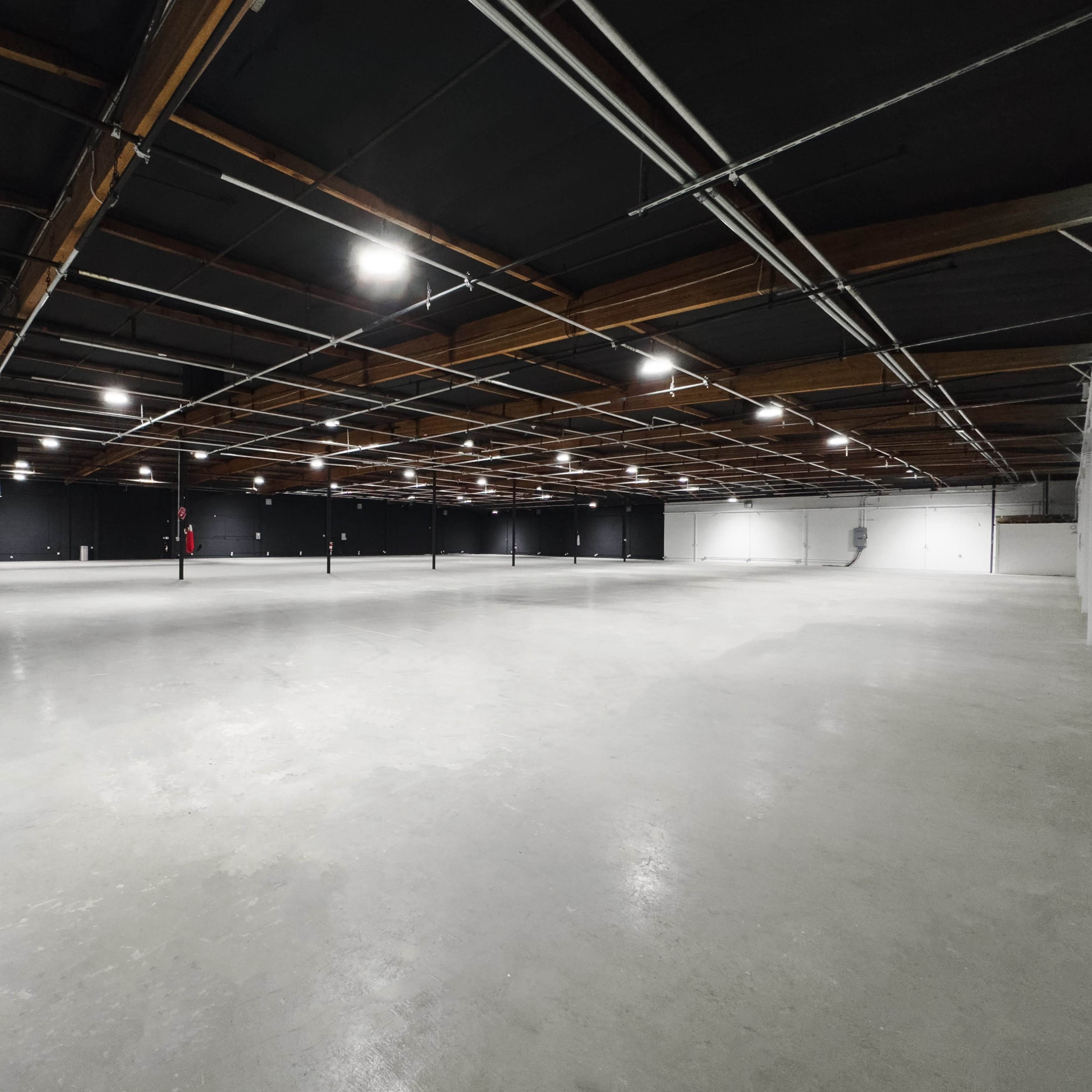 A large, empty warehouse space with a concrete floor and exposed lighting above.
