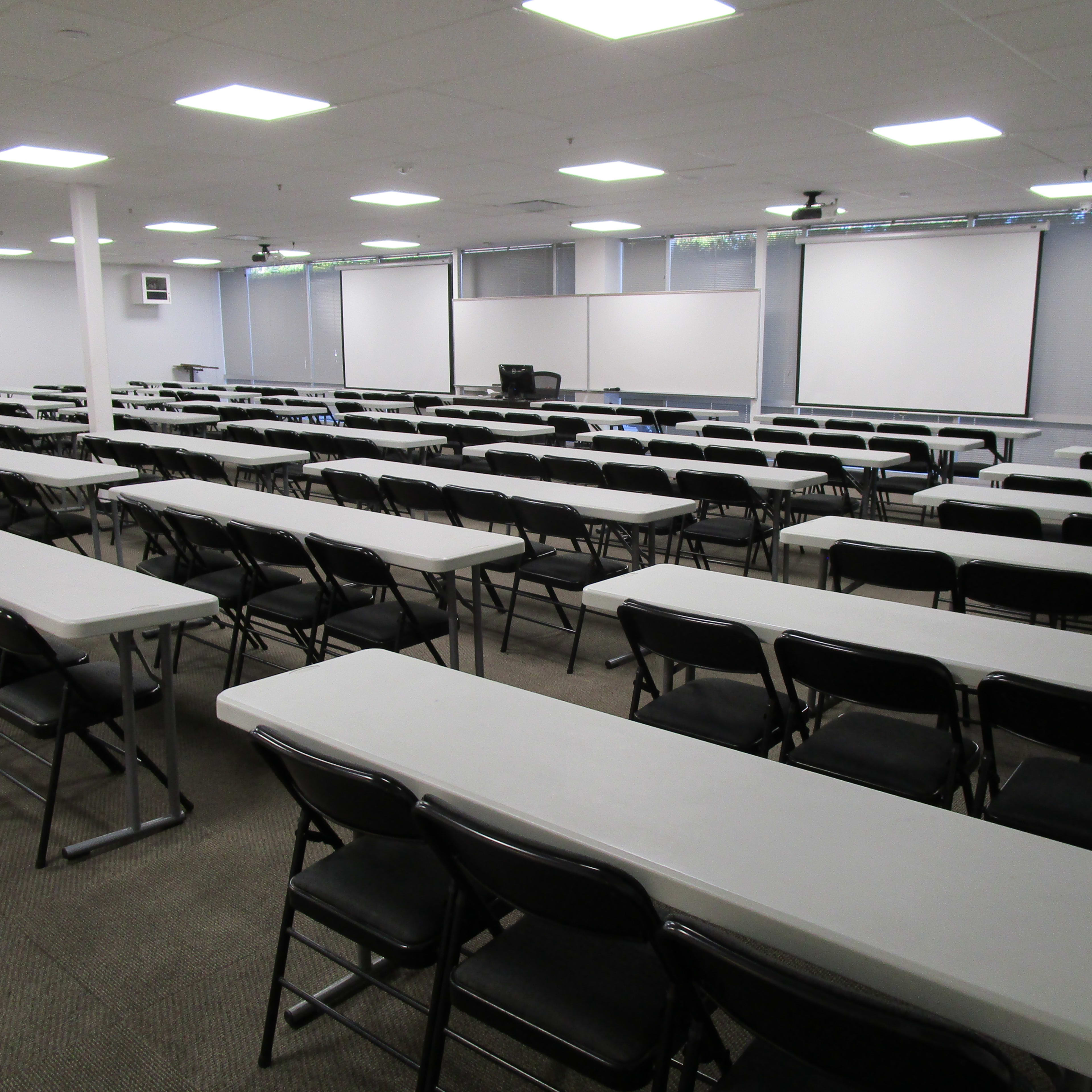 A large, empty classroom with rows of tables and chairs arranged for a meeting or training session.