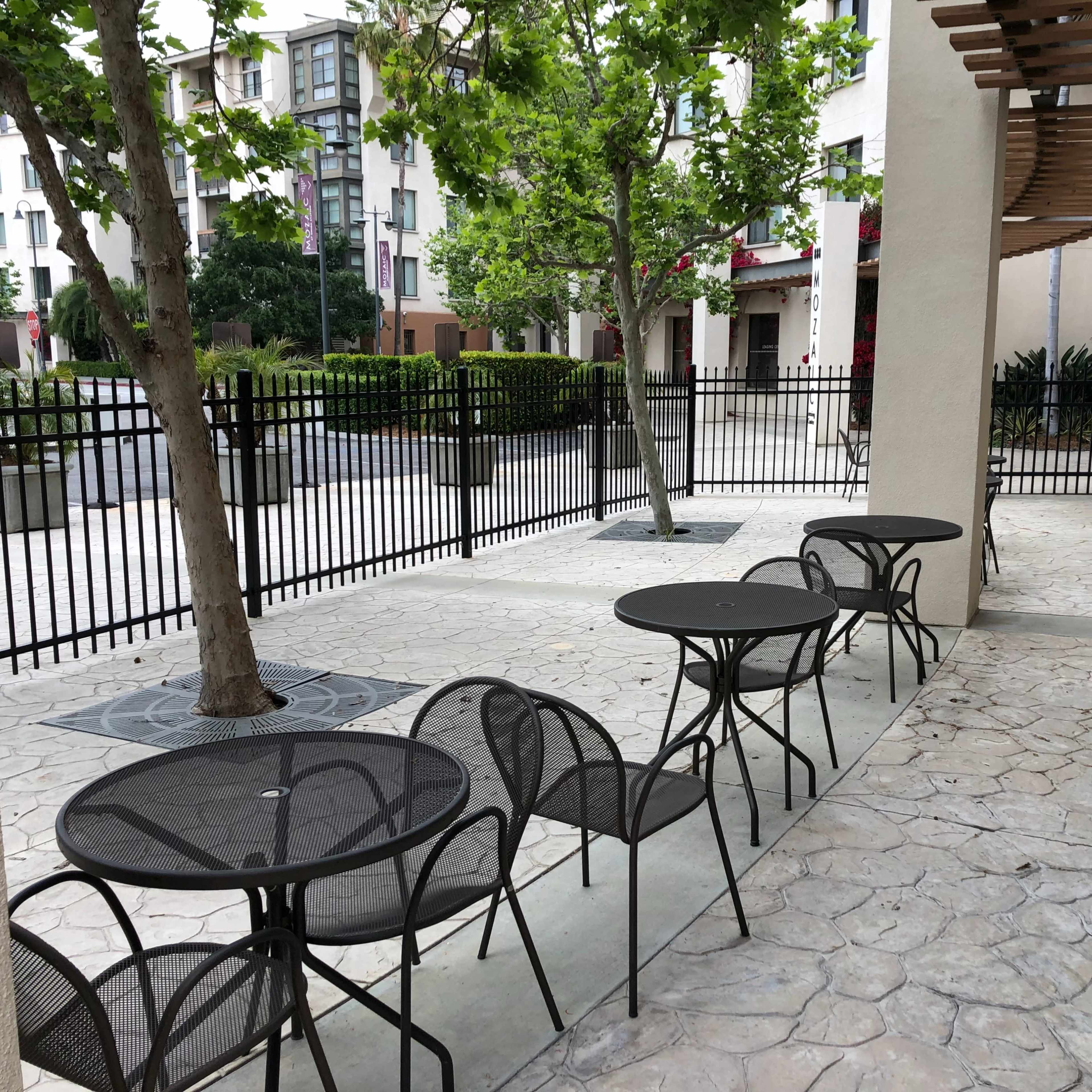A courtyard area with several black metal tables and chairs surrounded by trees and a fence.