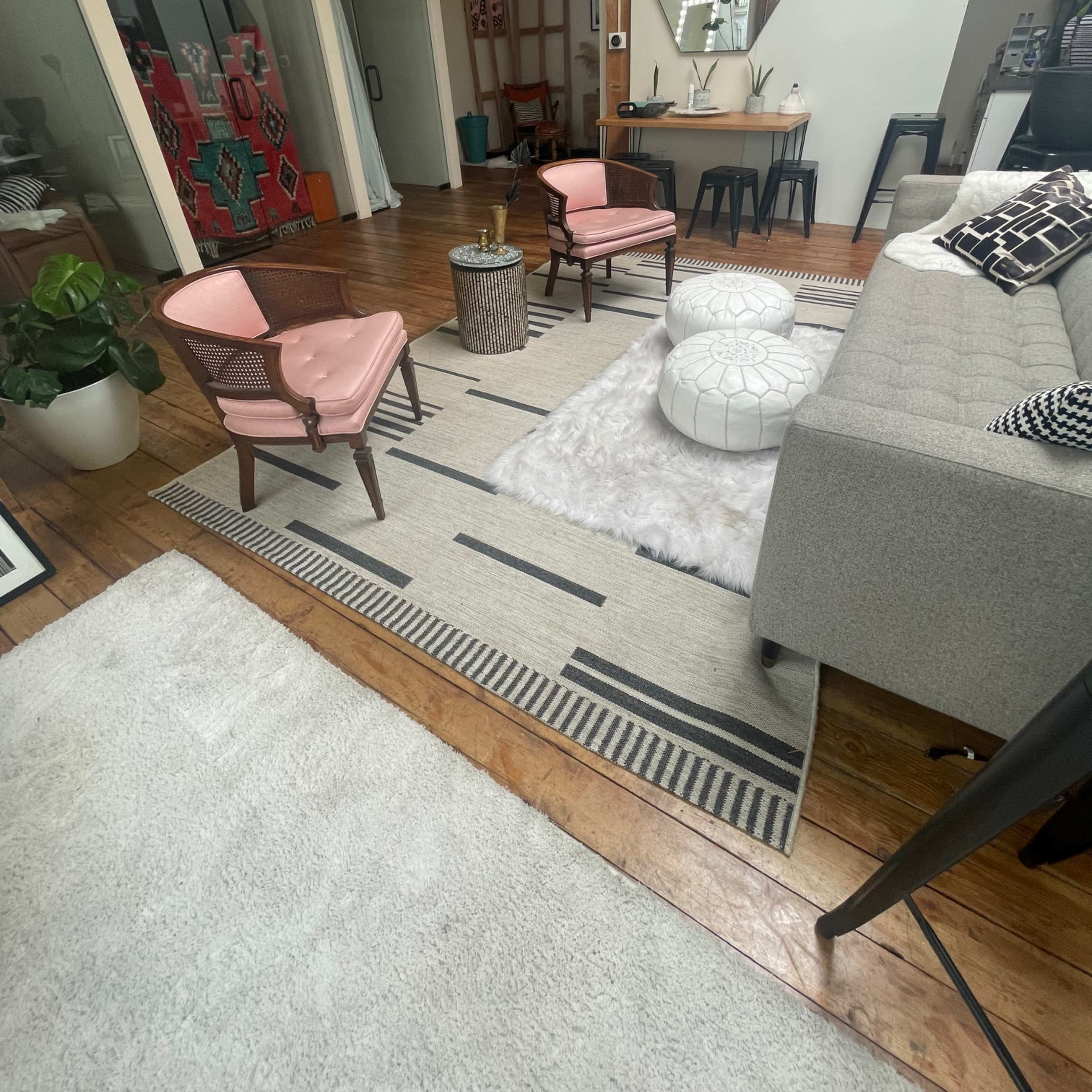 A modern living space featuring a gray sofa, two pink armchairs, a round coffee table on a patterned rug, and a white faux fur throw on the floor.
