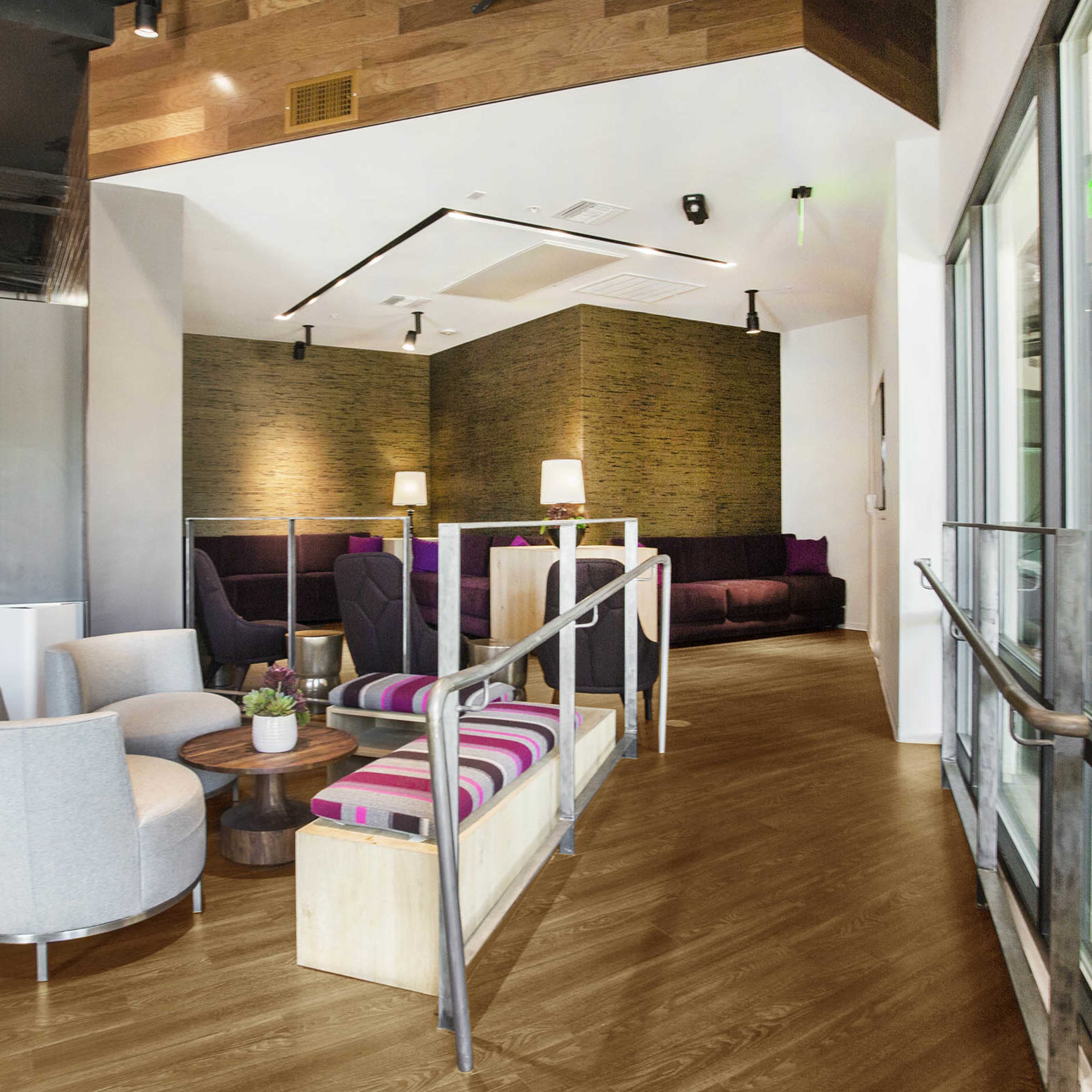 A modern interior space featuring a seating area with gray chairs and a wooden floor, alongside a bar counter and decorative lighting.