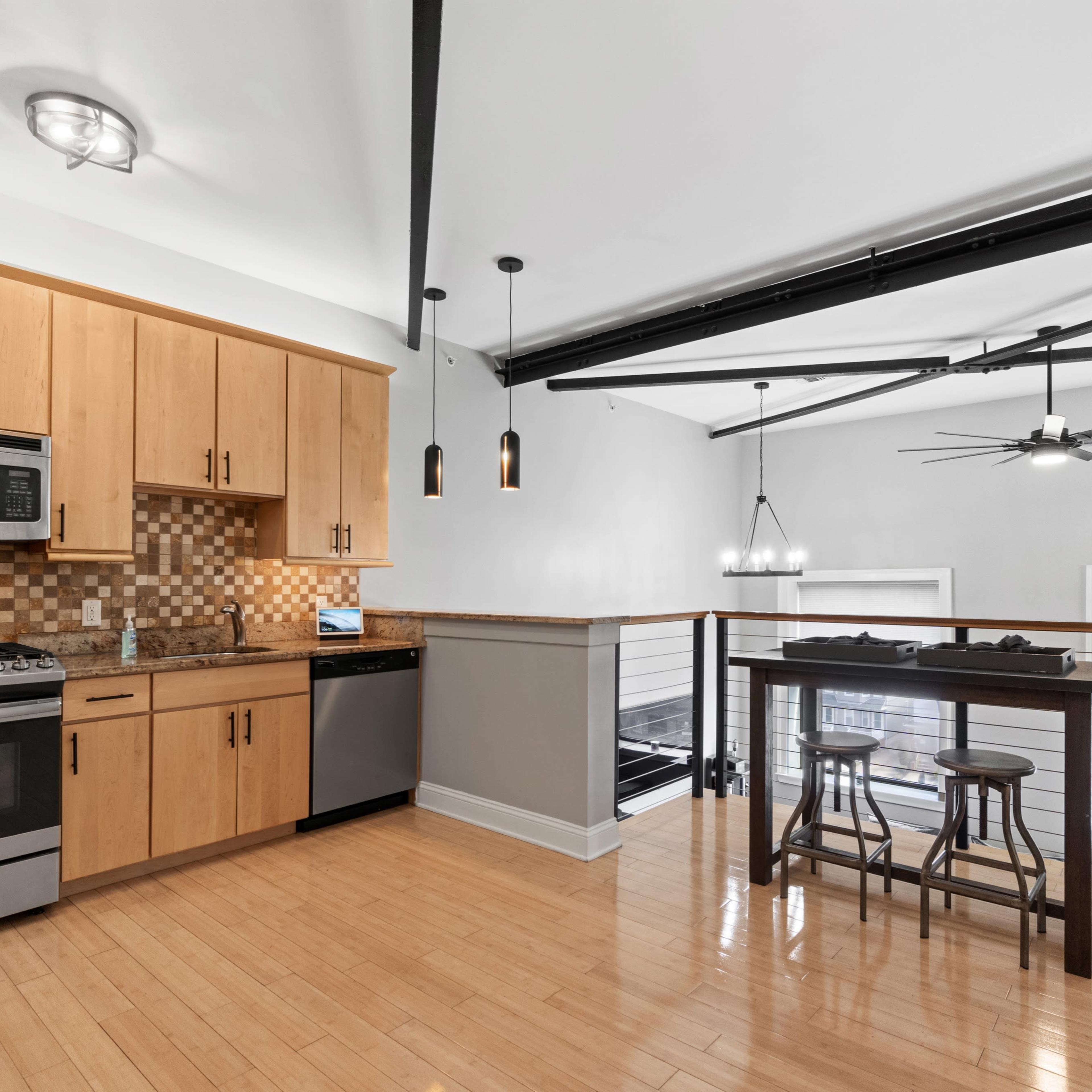 A modern kitchen with wooden cabinetry, stainless steel appliances, and a bar-height table with stools.