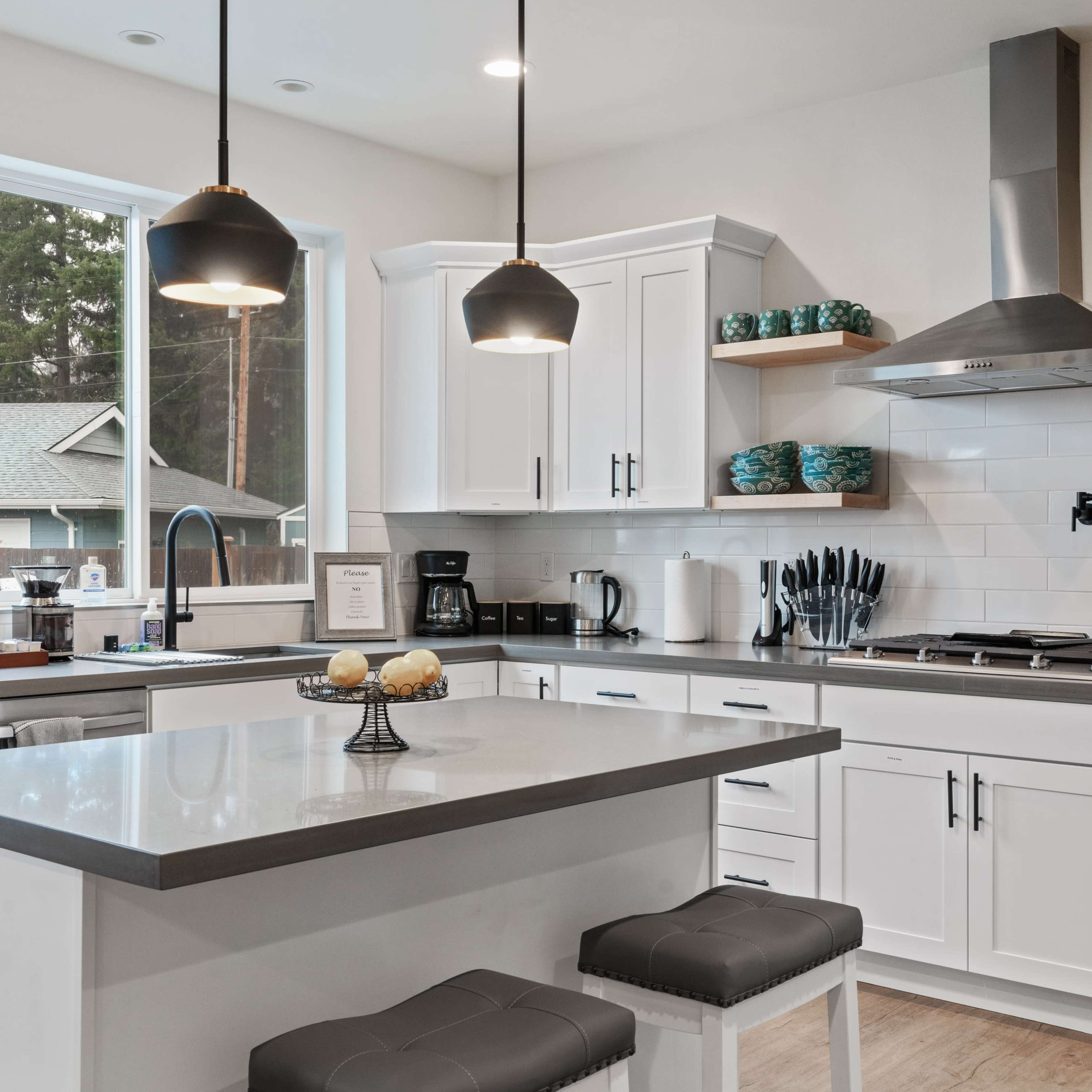 The kitchen features white cabinets, a gray island with stools, and stainless steel appliances, illuminated by pendant lights.