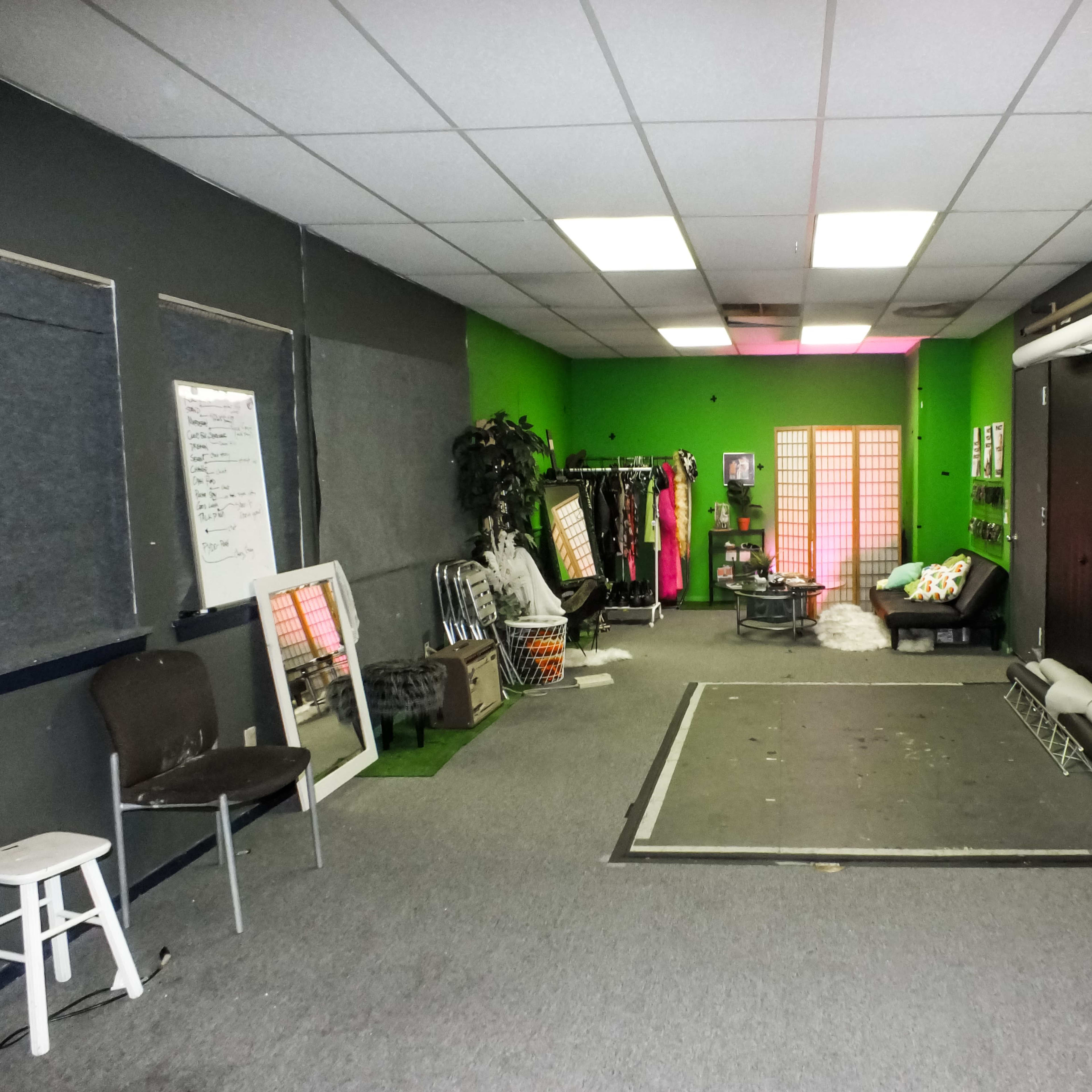 A spacious studio with gray carpet, green walls, and various clothing racks along one side.