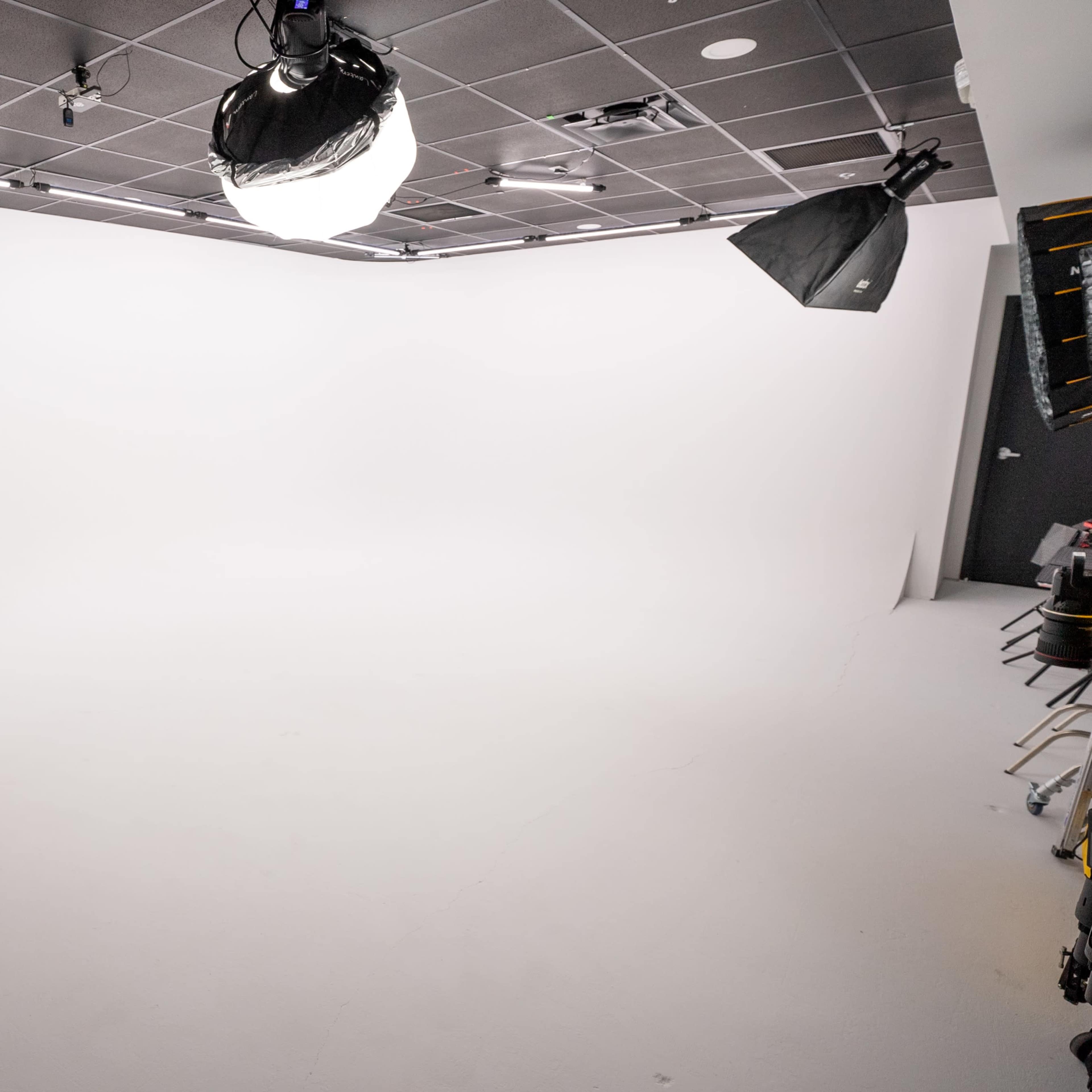 A studio space with a seamless white backdrop and multiple lighting fixtures positioned overhead.