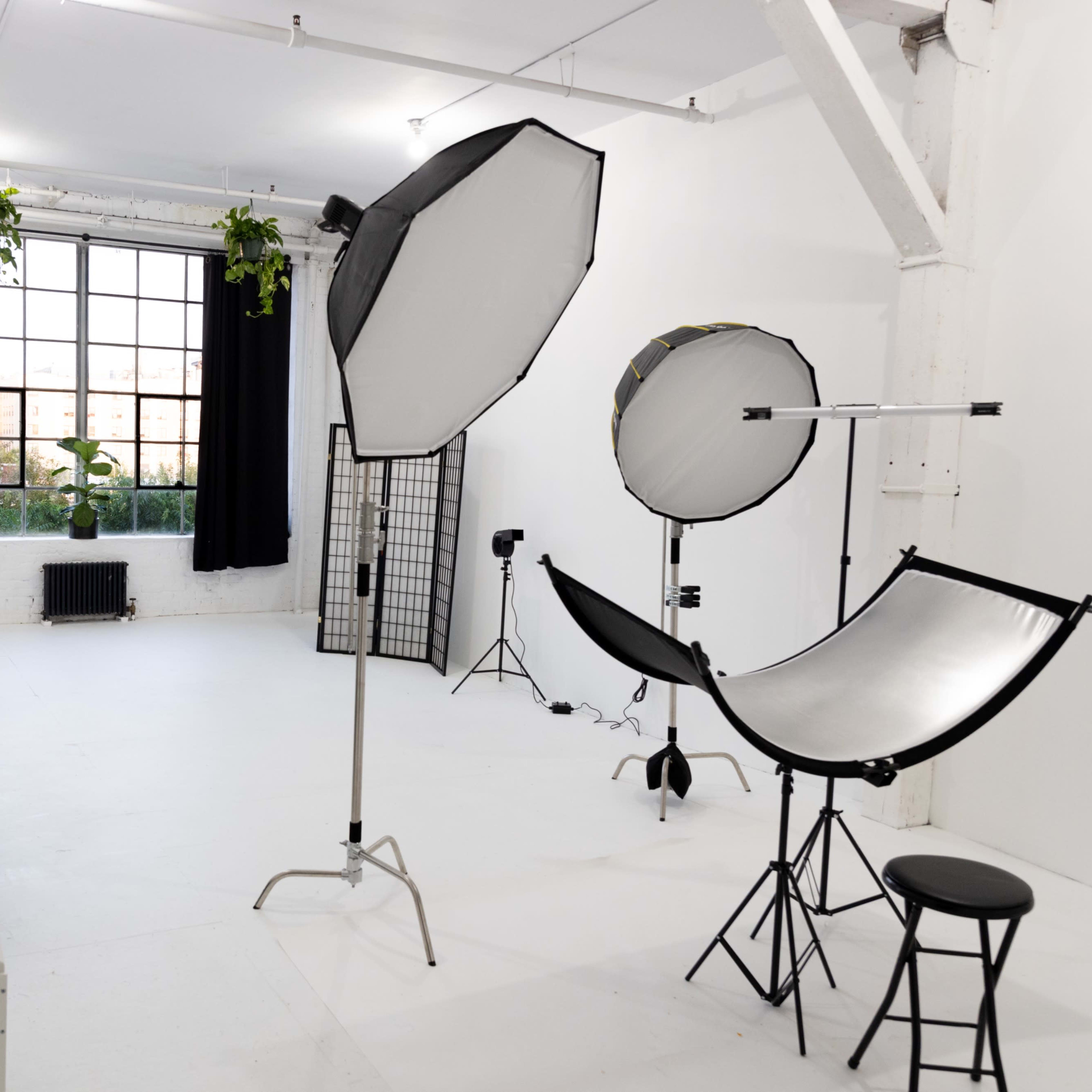A photography studio featuring backdrop stands, light sources, and a seating area with a mirror.