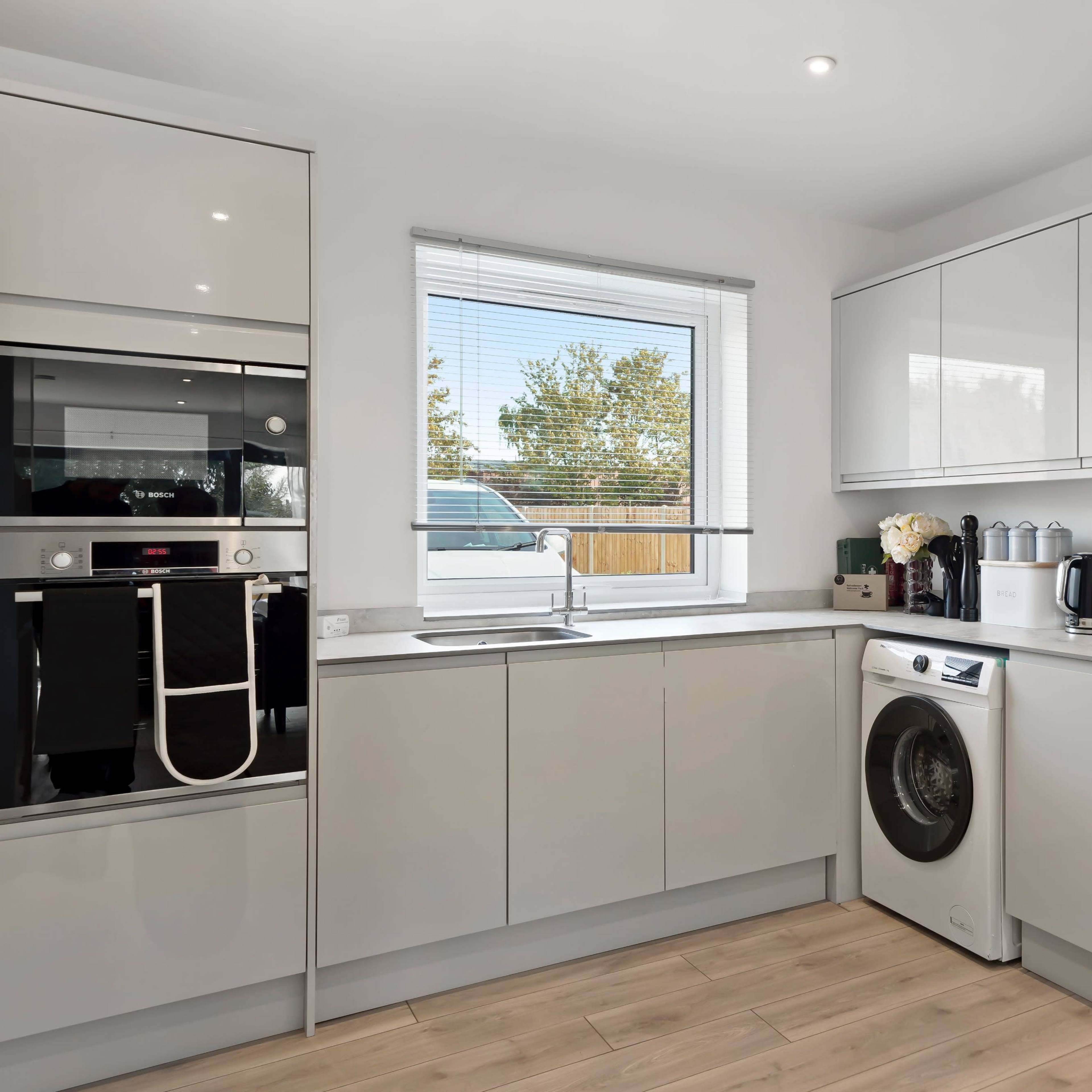 A modern kitchen features sleek cabinetry, a window with a view, and various appliances, including a washing machine and cooking pots.
