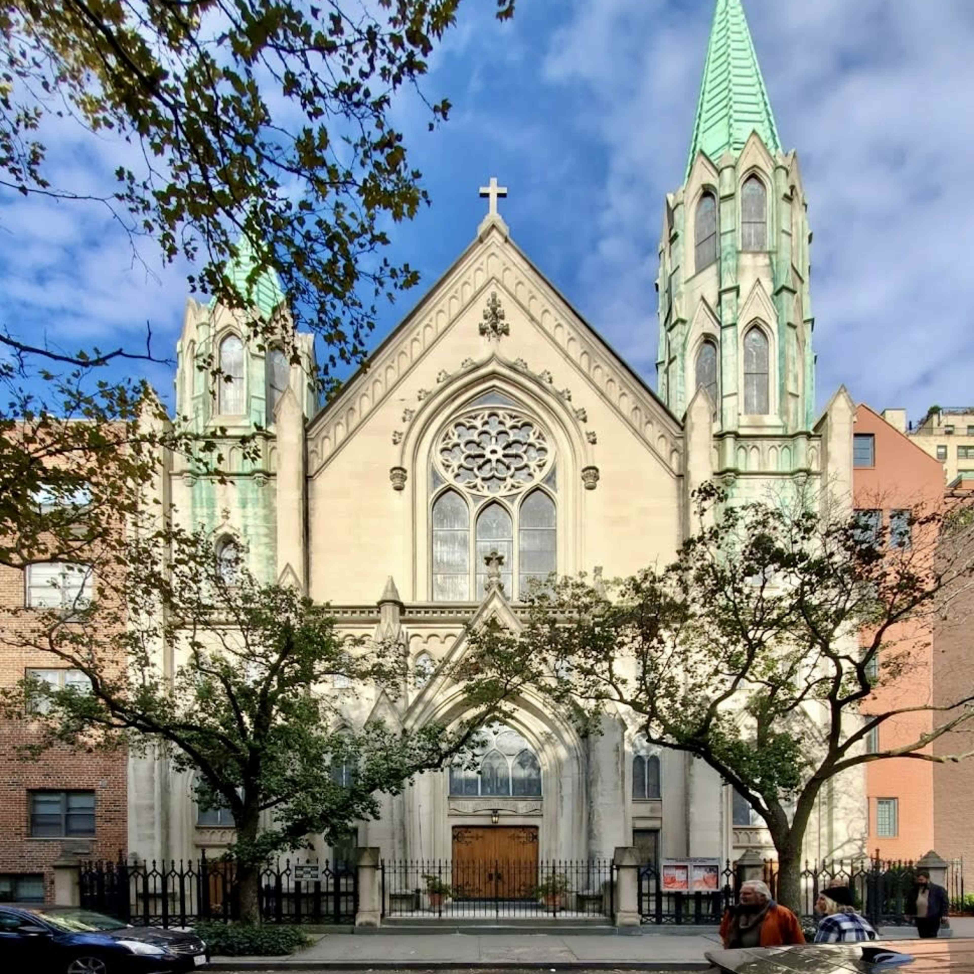 A large church with a Gothic architectural style featuring two tall spires and a large rose window, surrounded by trees and buildings.