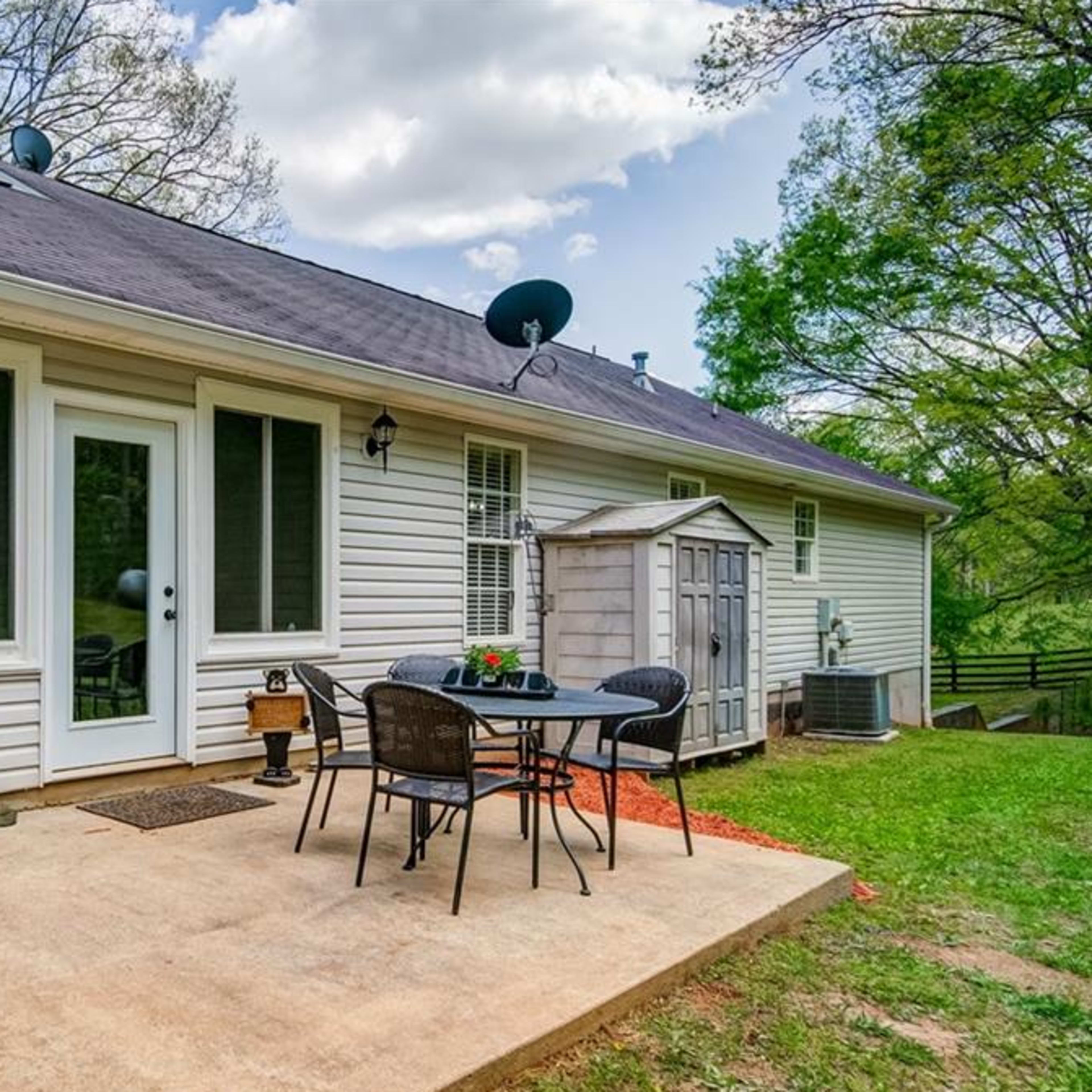 A patio area with a table and chairs outside a house, alongside a small storage shed and grassy surroundings.