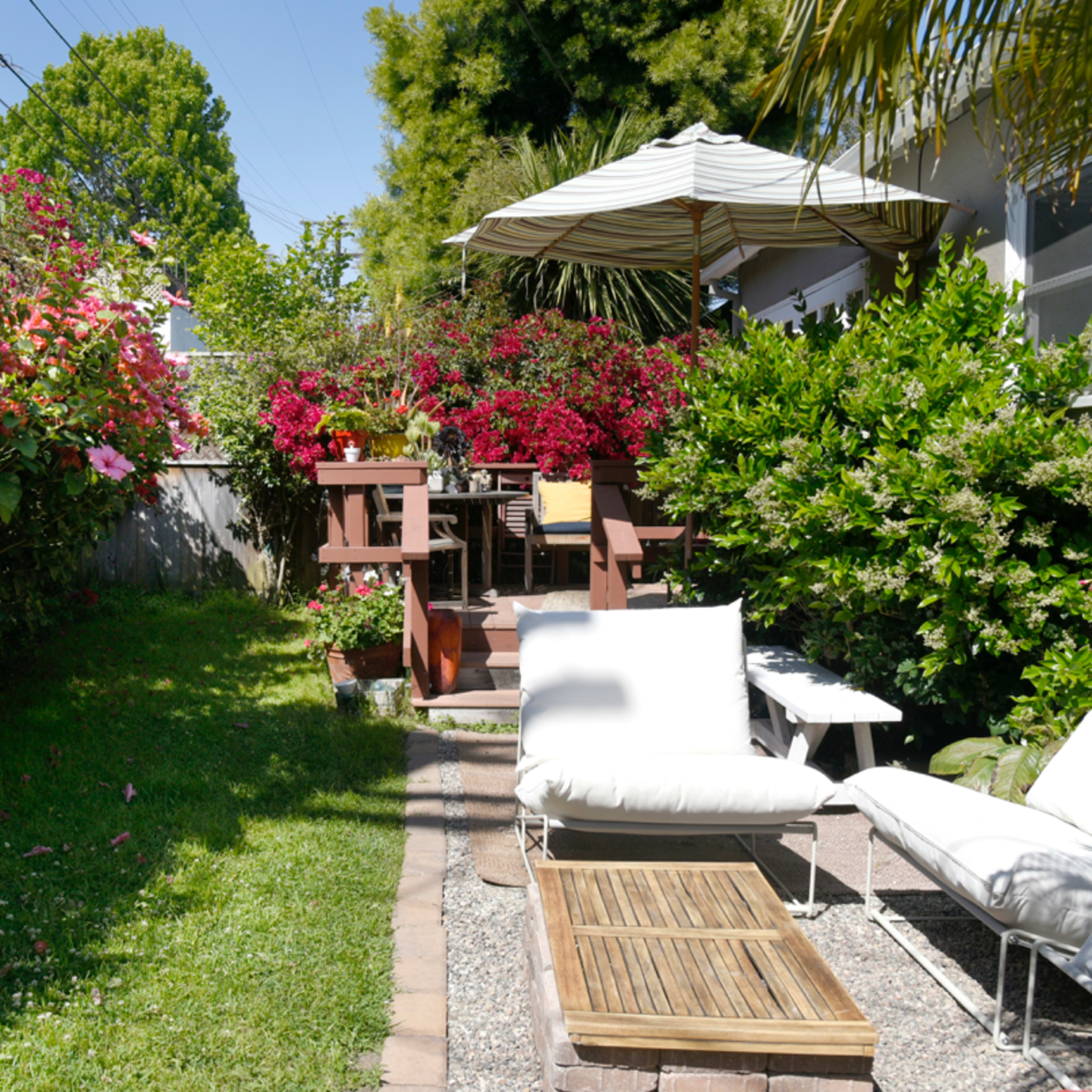 A garden area with blooming flowers, a patio set, and two lounge chairs on a grassy patch.