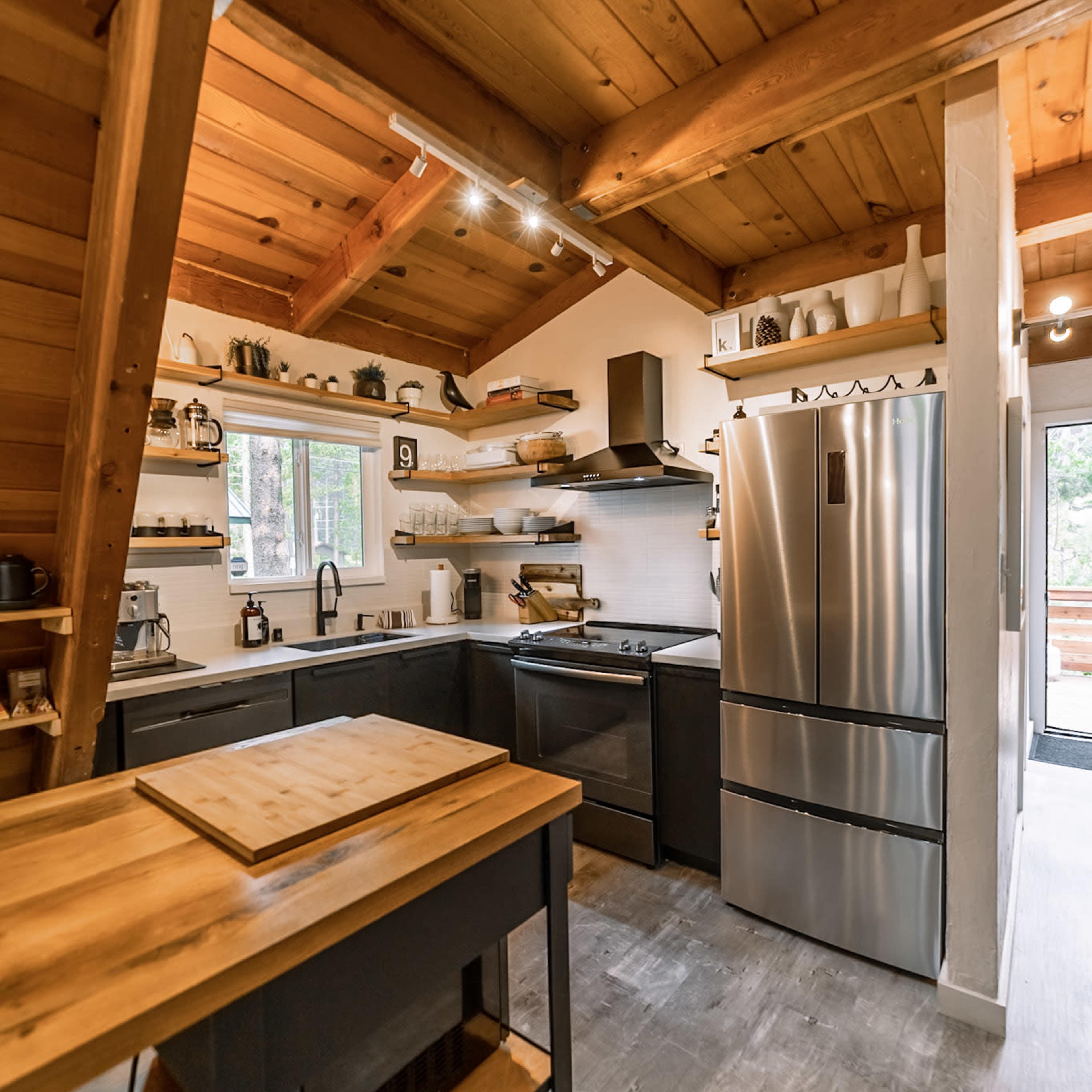 A modern kitchen features stainless steel appliances, wooden beams, and open shelving with various kitchenware.