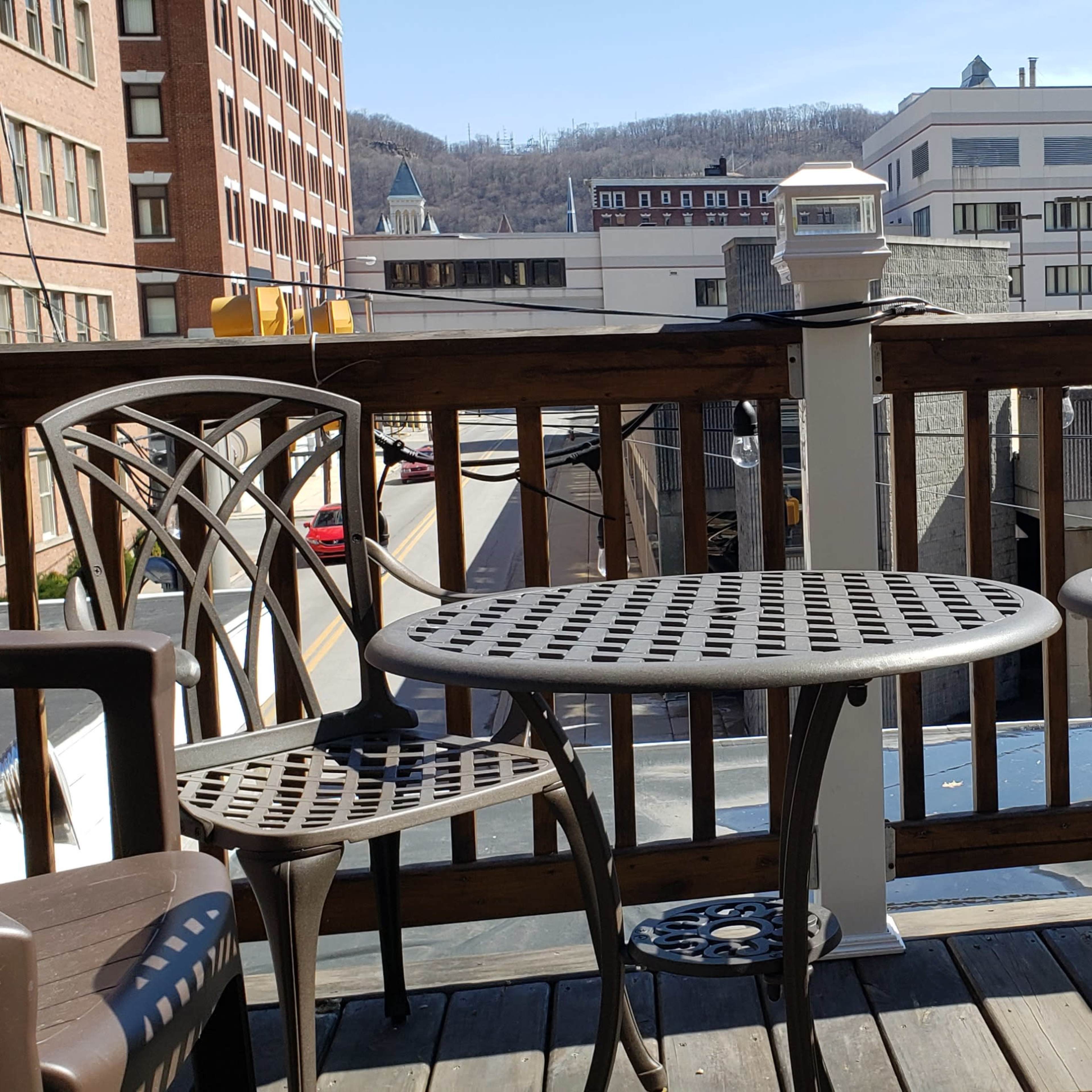 A wooden deck with two round metal tables and four chairs overlooking a city street and buildings in the background.