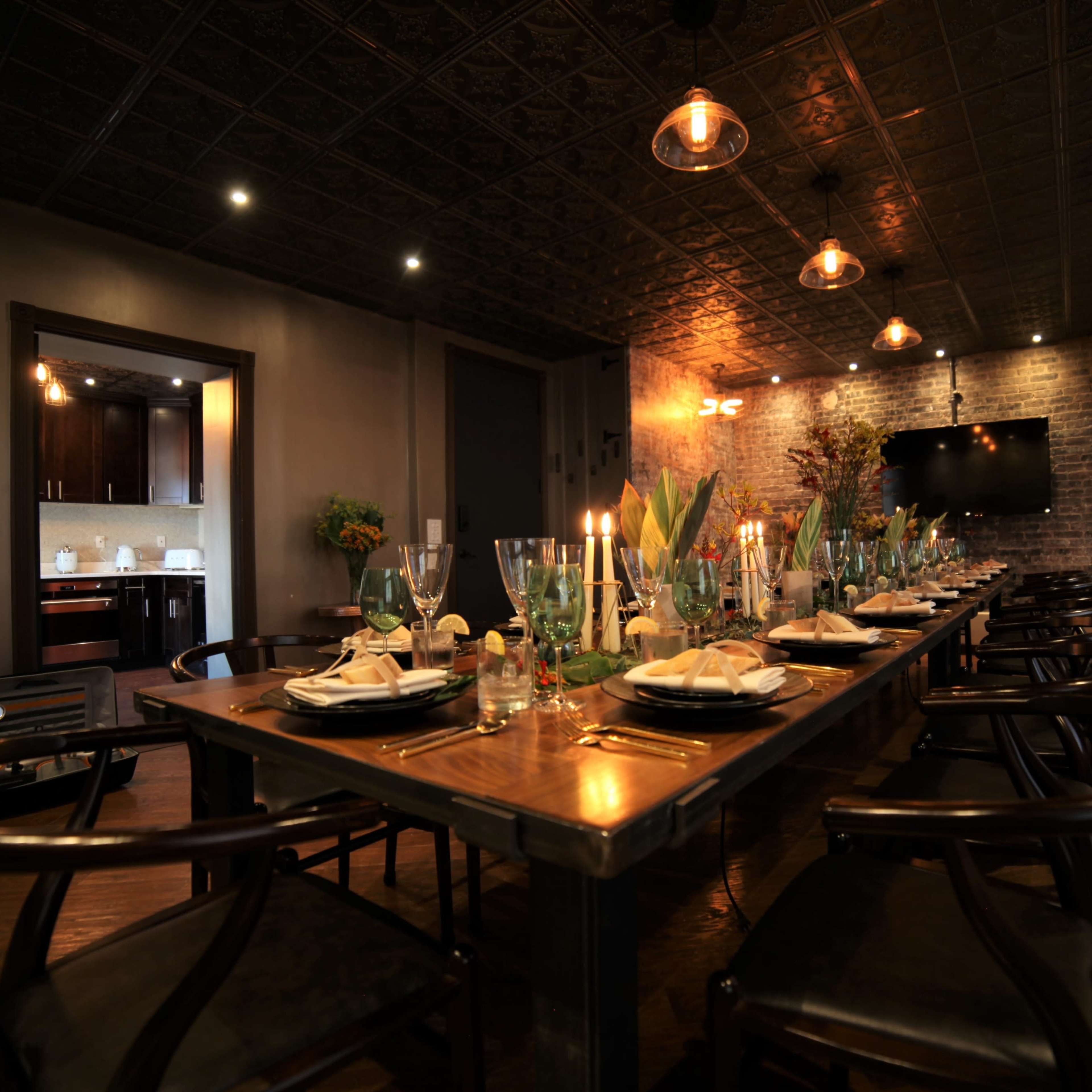 A long dining table set with plates, glasses, and candles in a modern restaurant with exposed brick walls and dim lighting.