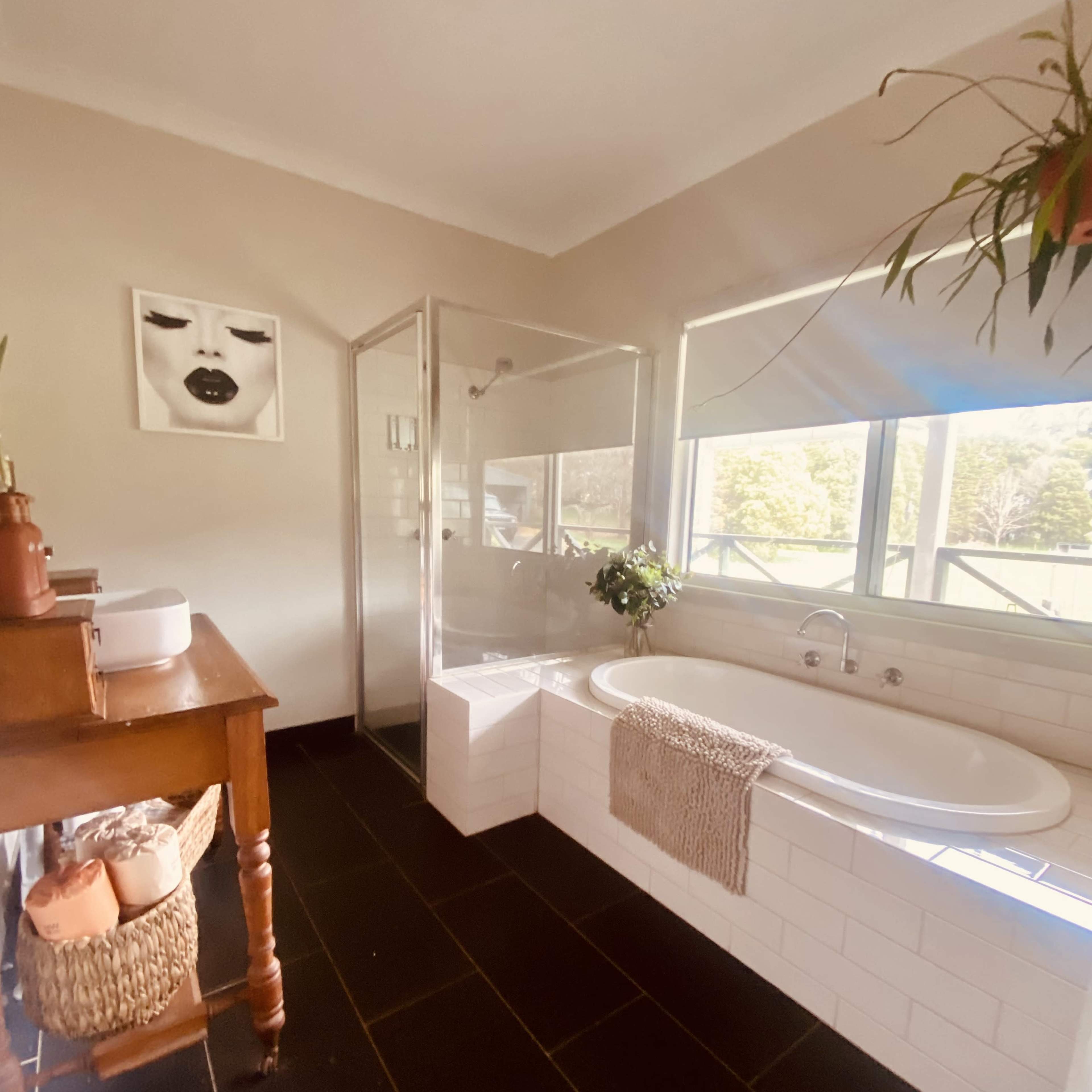 The bathroom features a glass shower, a freestanding bathtub, and a wooden table with decorative items.