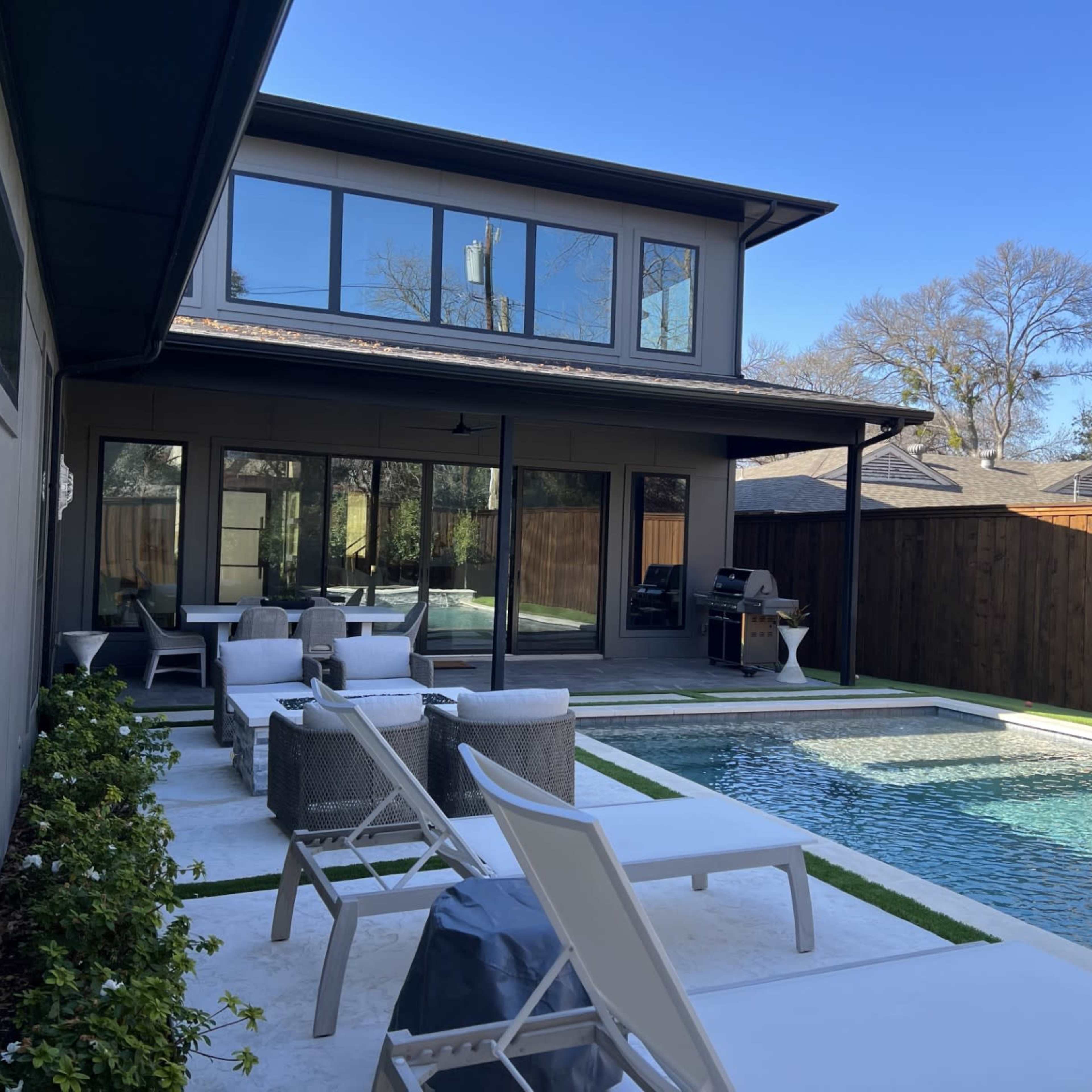A modern backyard with a swimming pool, lounge chairs, and a two-story house in the background.