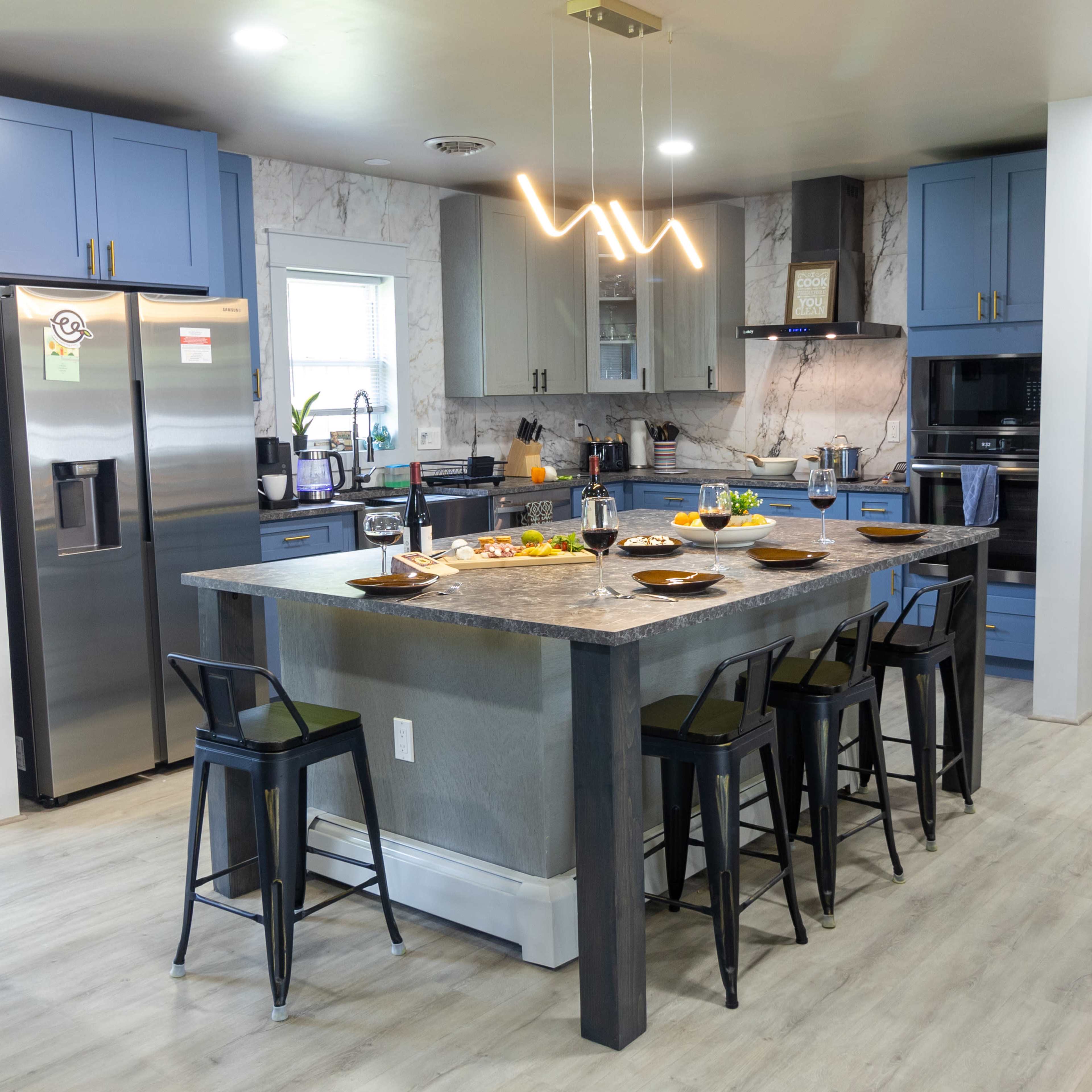 A modern kitchen featuring a large island with seating, stainless steel appliances, and blue cabinetry.