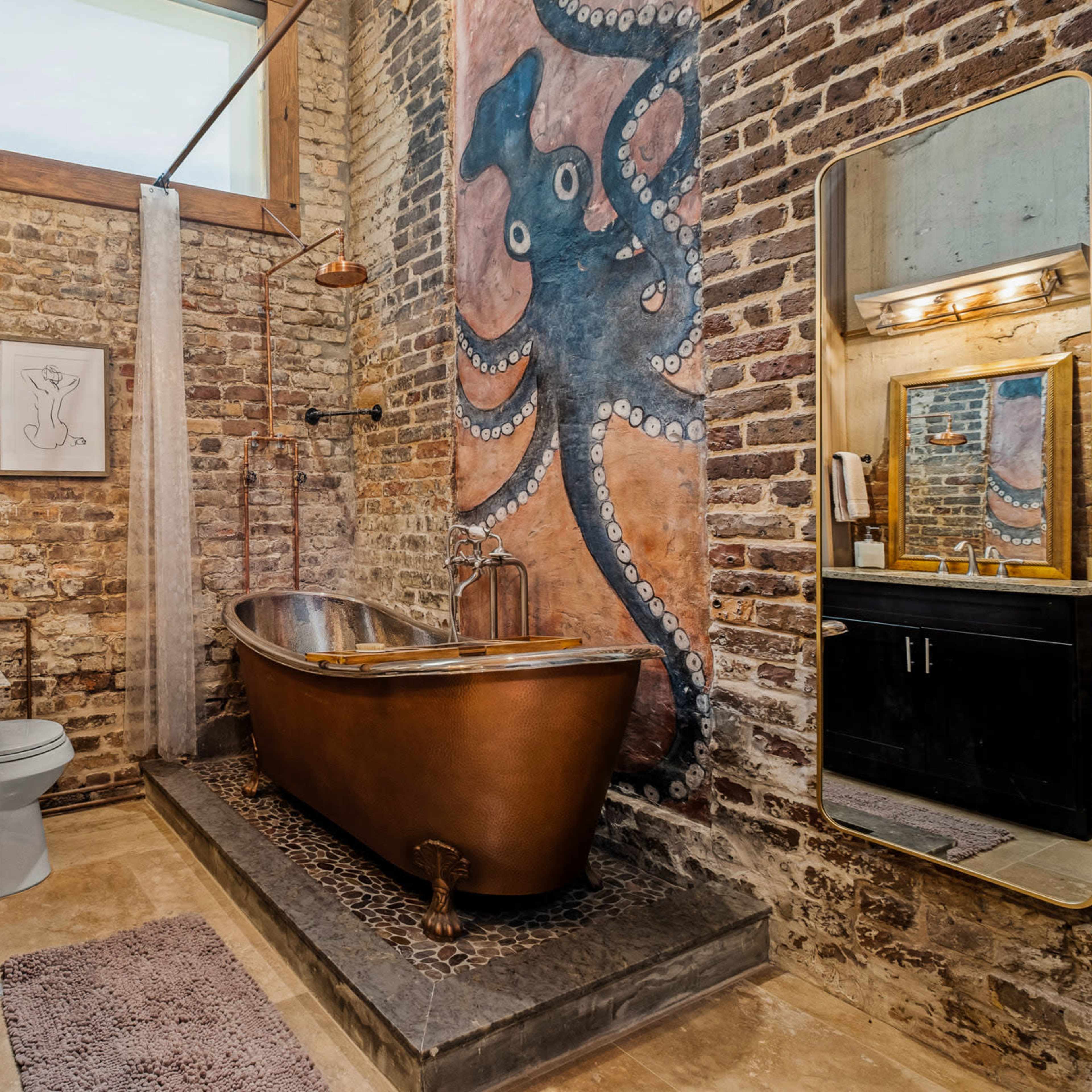A rustic bathroom featuring a vintage copper bathtub, a brick wall with an octopus mural, and a modern sink vanity.