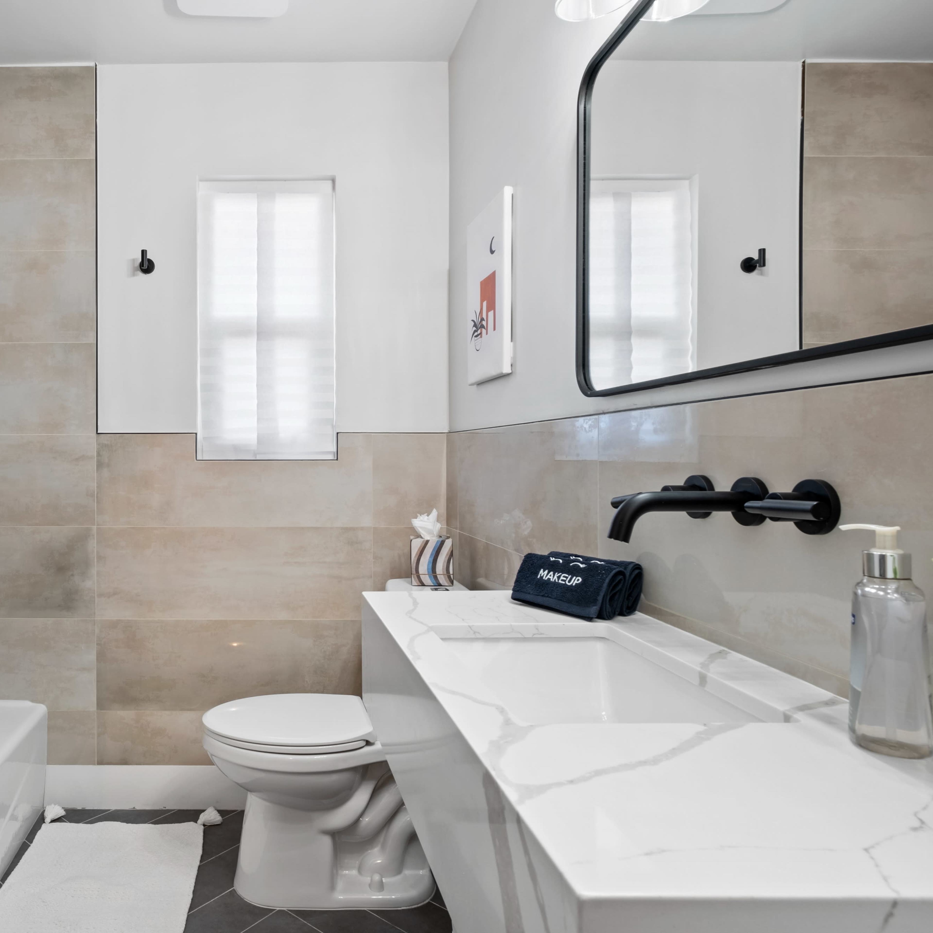 A modern bathroom featuring a shower with a glass enclosure, a white toilet, a marble-top vanity with a sink, and neutral-colored tile walls.
